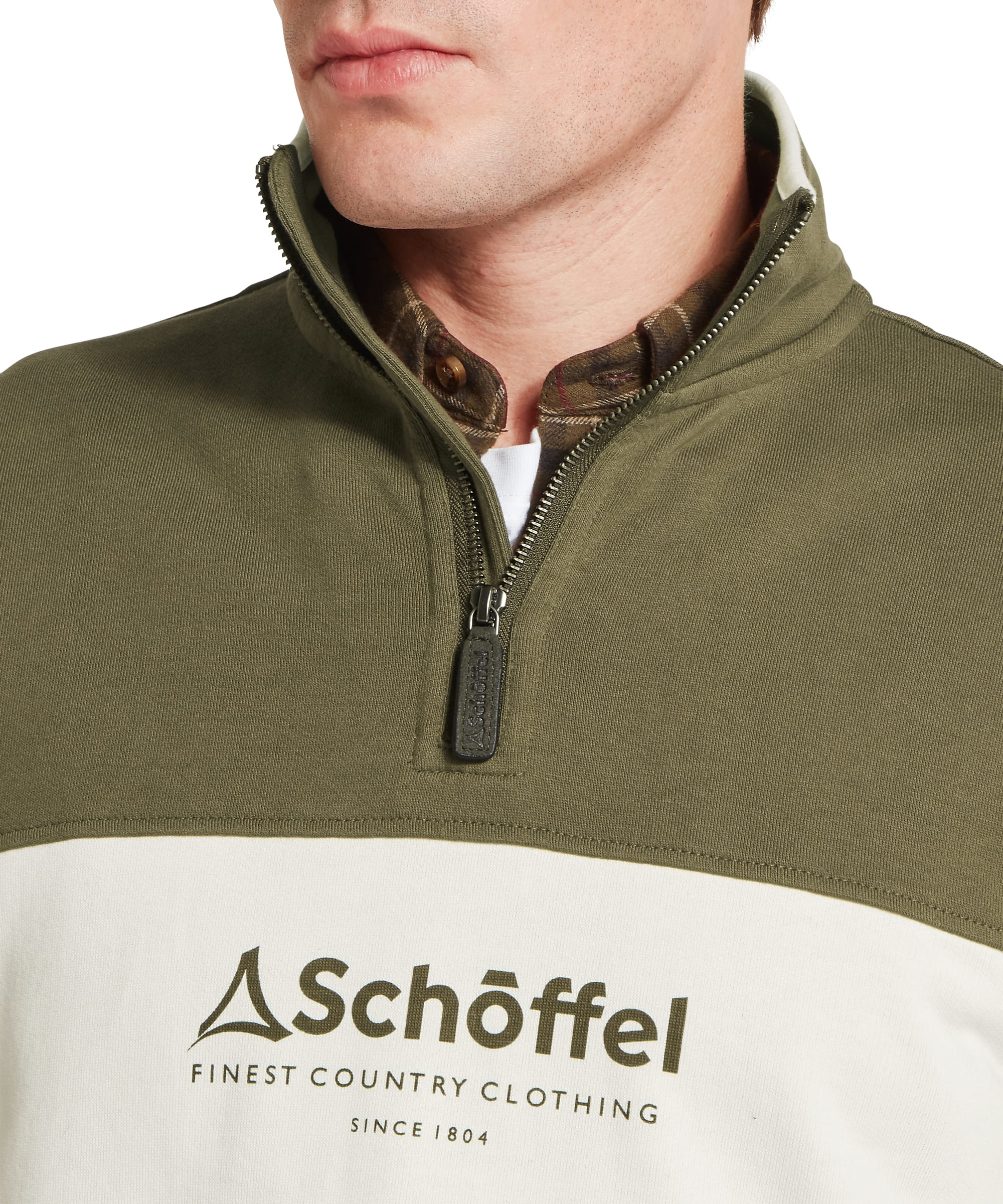 Schöffel Men's Trencrom ¼ Zip in olive green — close-up of the chest showing the Schöffel "Finest Country Clothing Since 1804" heritage logo printed on the ecru colour-block panel, with the olive quarter-zip stand collar above