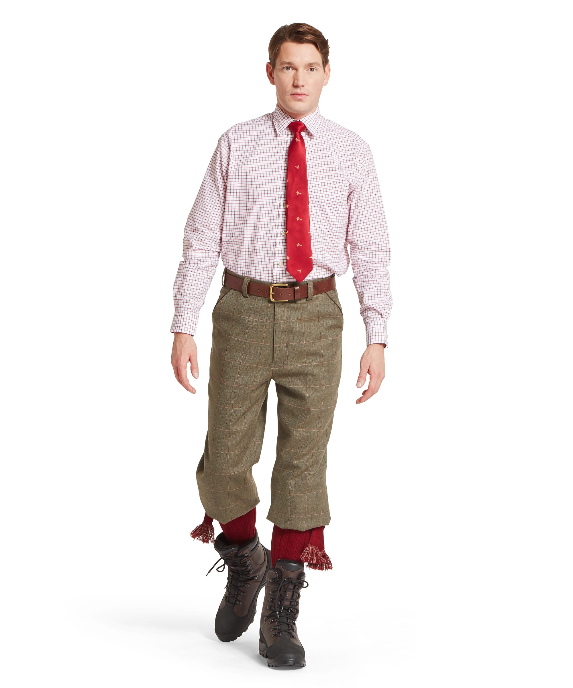 Man wearing a red tie, pink shirt, green tweed plus fours, and brown boots on a white background