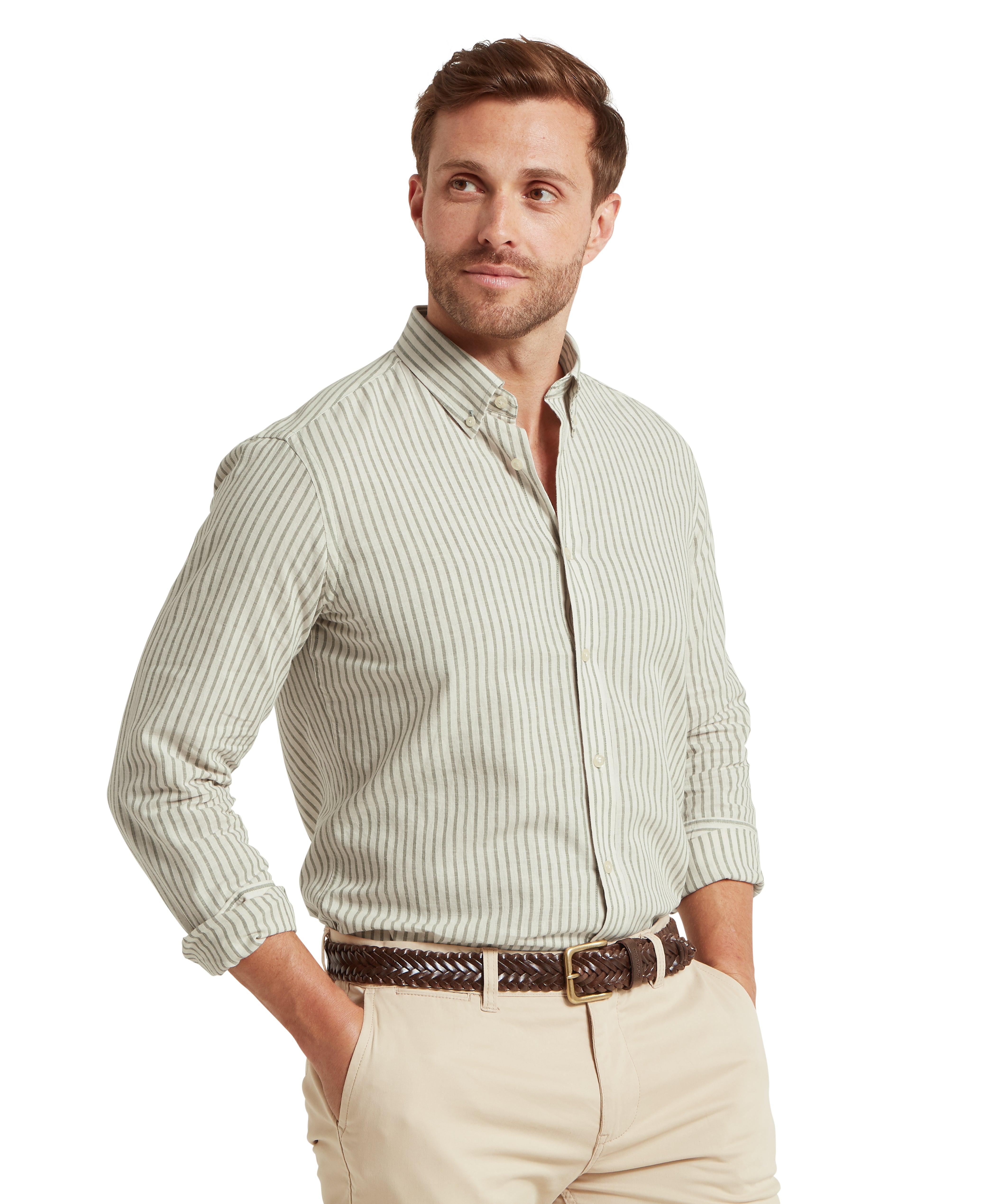 Man wearing a light green striped shirt and beige trousers against a white background.  The man is looking to the side with both hands in his pockets.