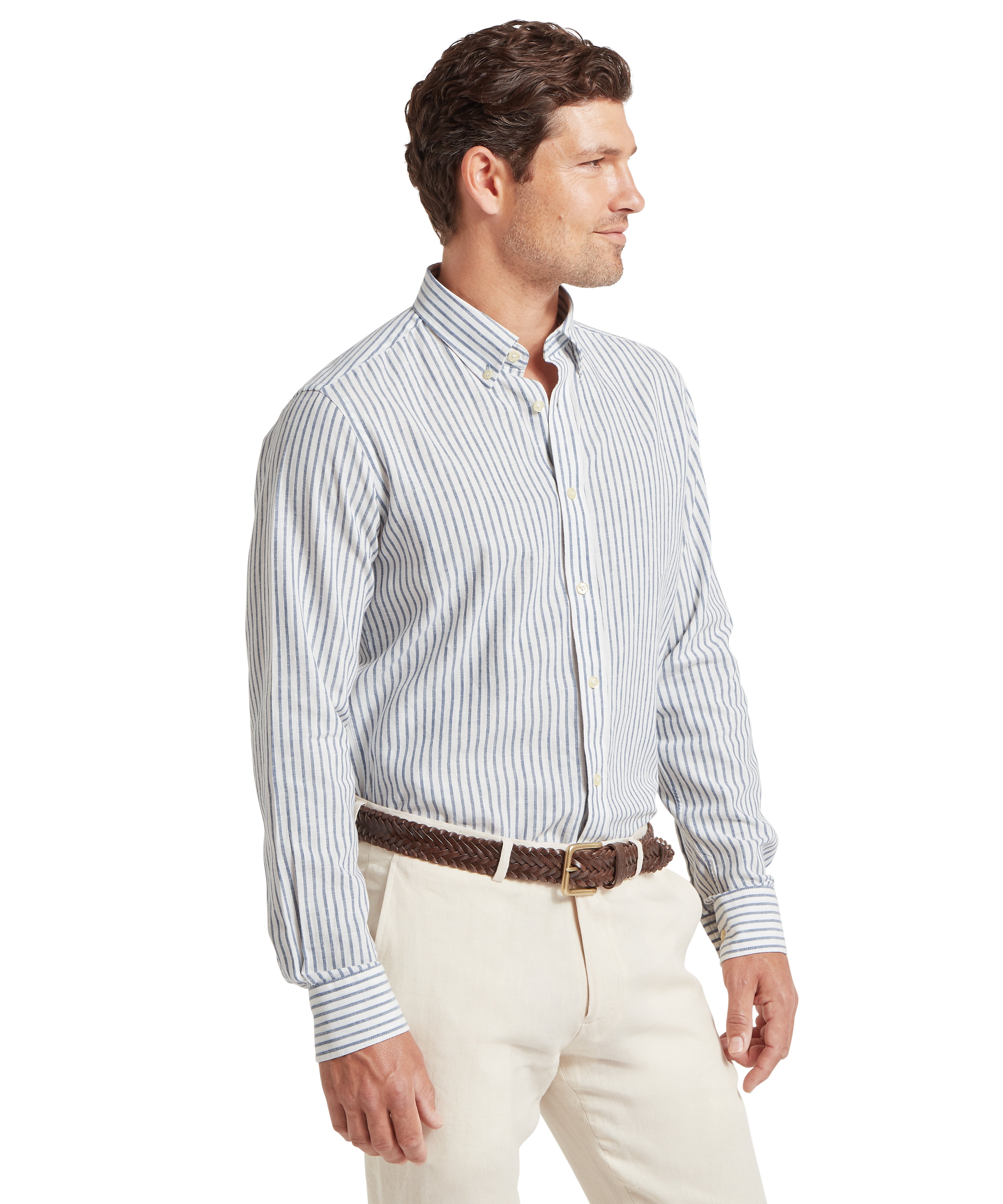 A man standing in a three-quarter profile wearing a long-sleeve, button-up shirt with vertical blue and white stripes, tucked into light beige trousers. He has a brown braided belt and short, neatly styled brown hair. The background is plain white.