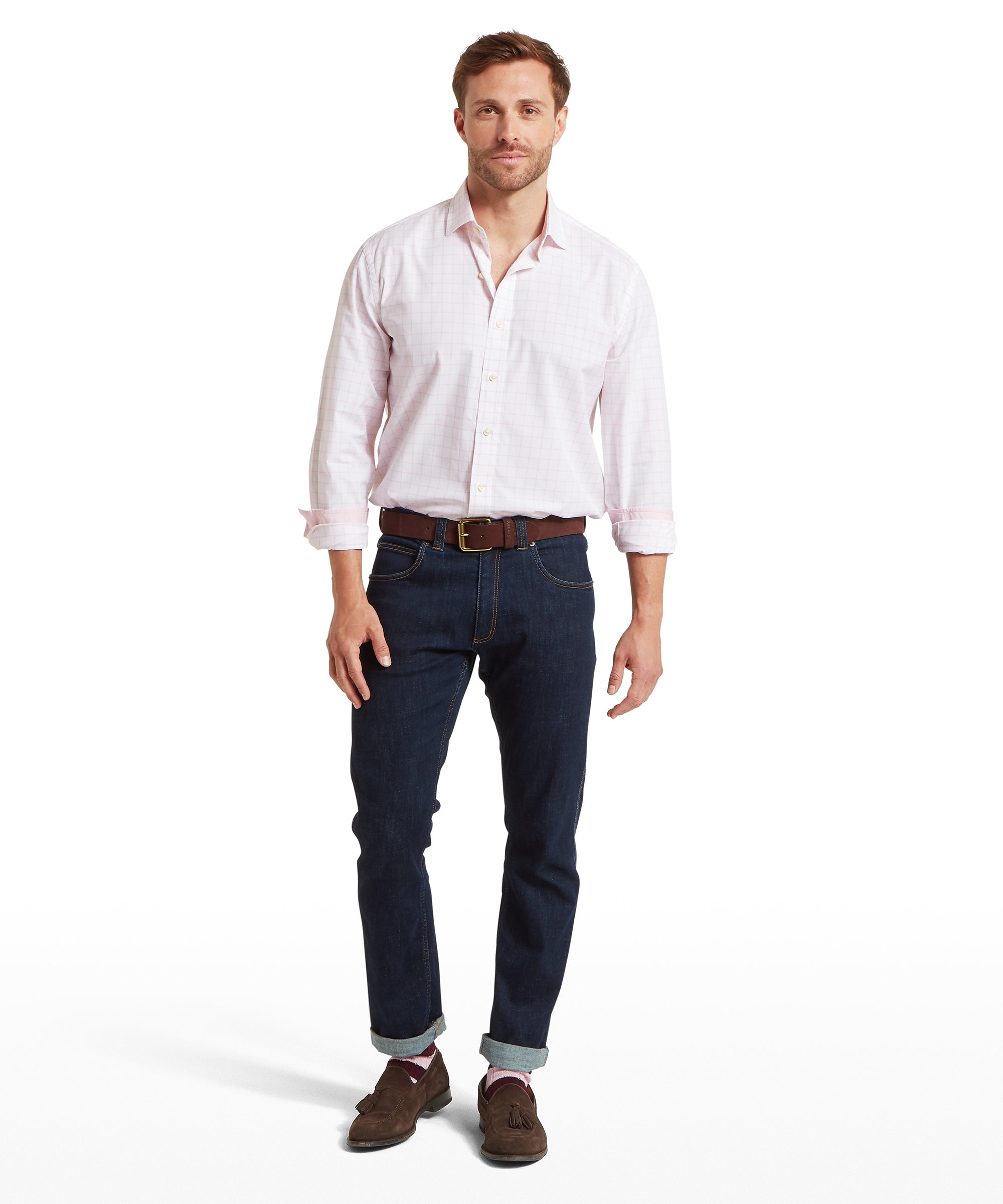 Man wearing a white and pink checked shirt, dark jeans, and brown shoes on a white background