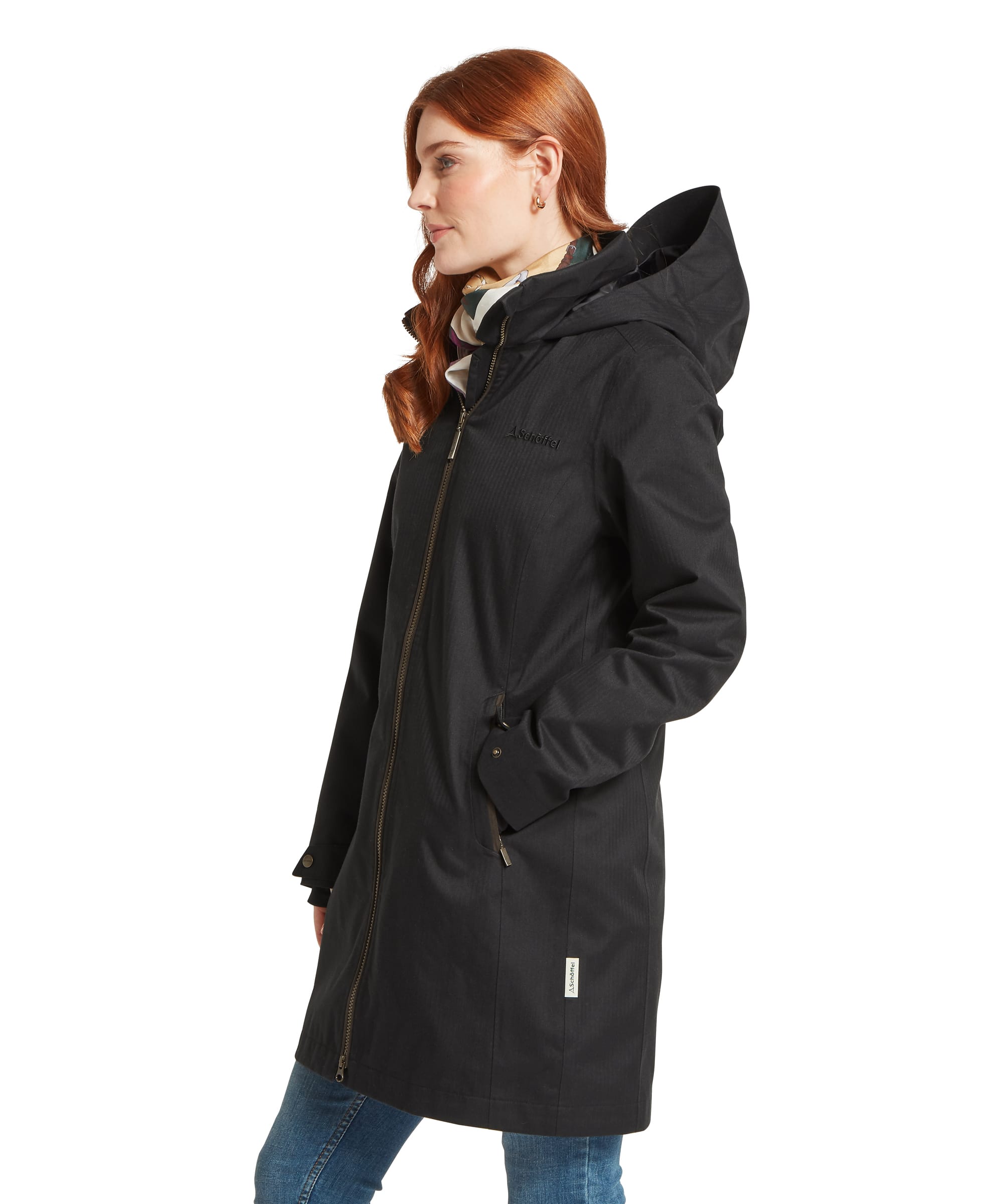 Side view of the Women's Schöffel Allexton Waterproof Coat in charcoal grey herringbone, featuring a full-length zip fastening, adjustable hood, zip pockets and Schöffel branding, styled over a silk equestrian-print scarf and blue jeans.