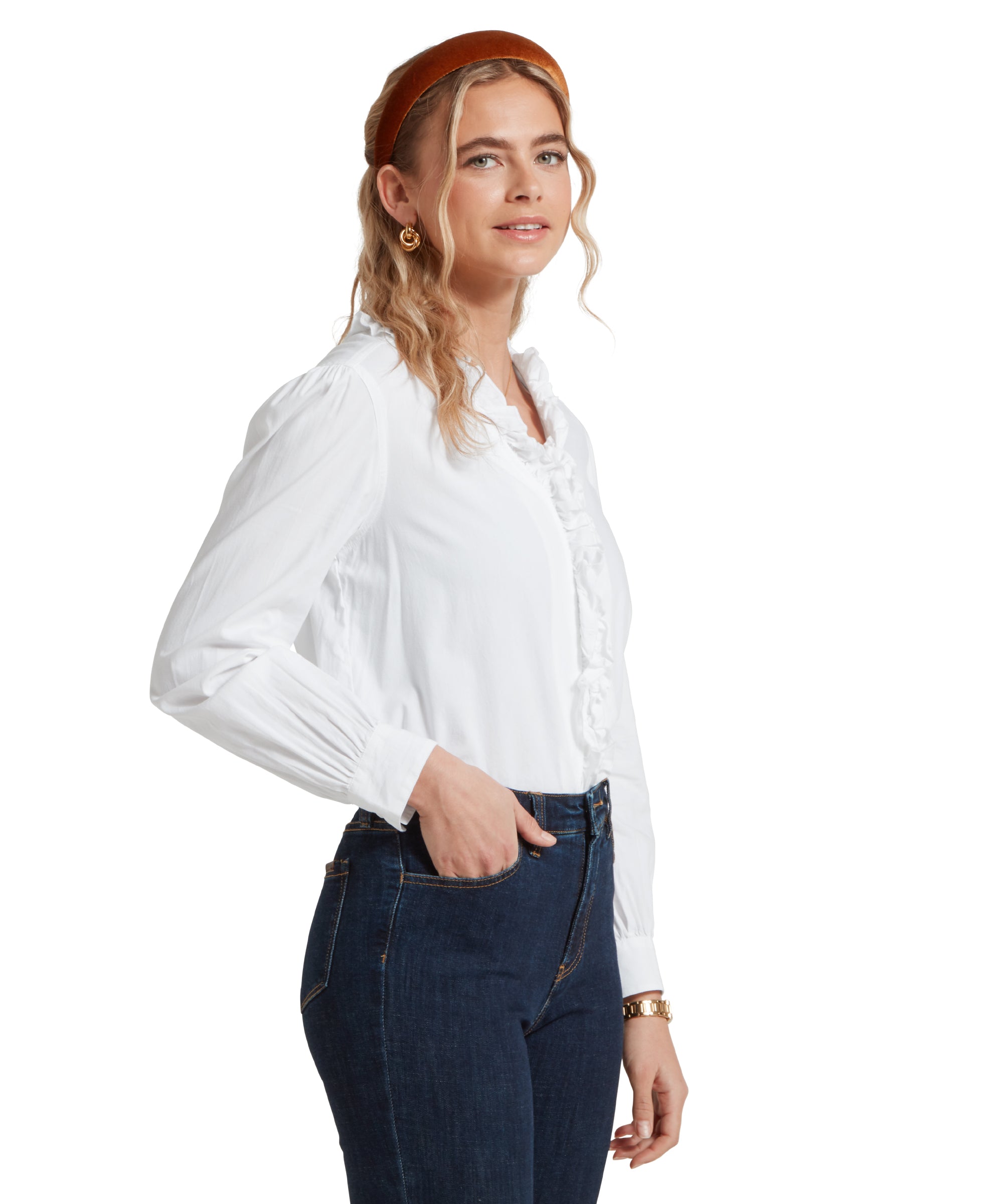 Side profile image of a female model wearing a tucked in white Schöffel shirt, paired with dark denim jeans and gold accessories.