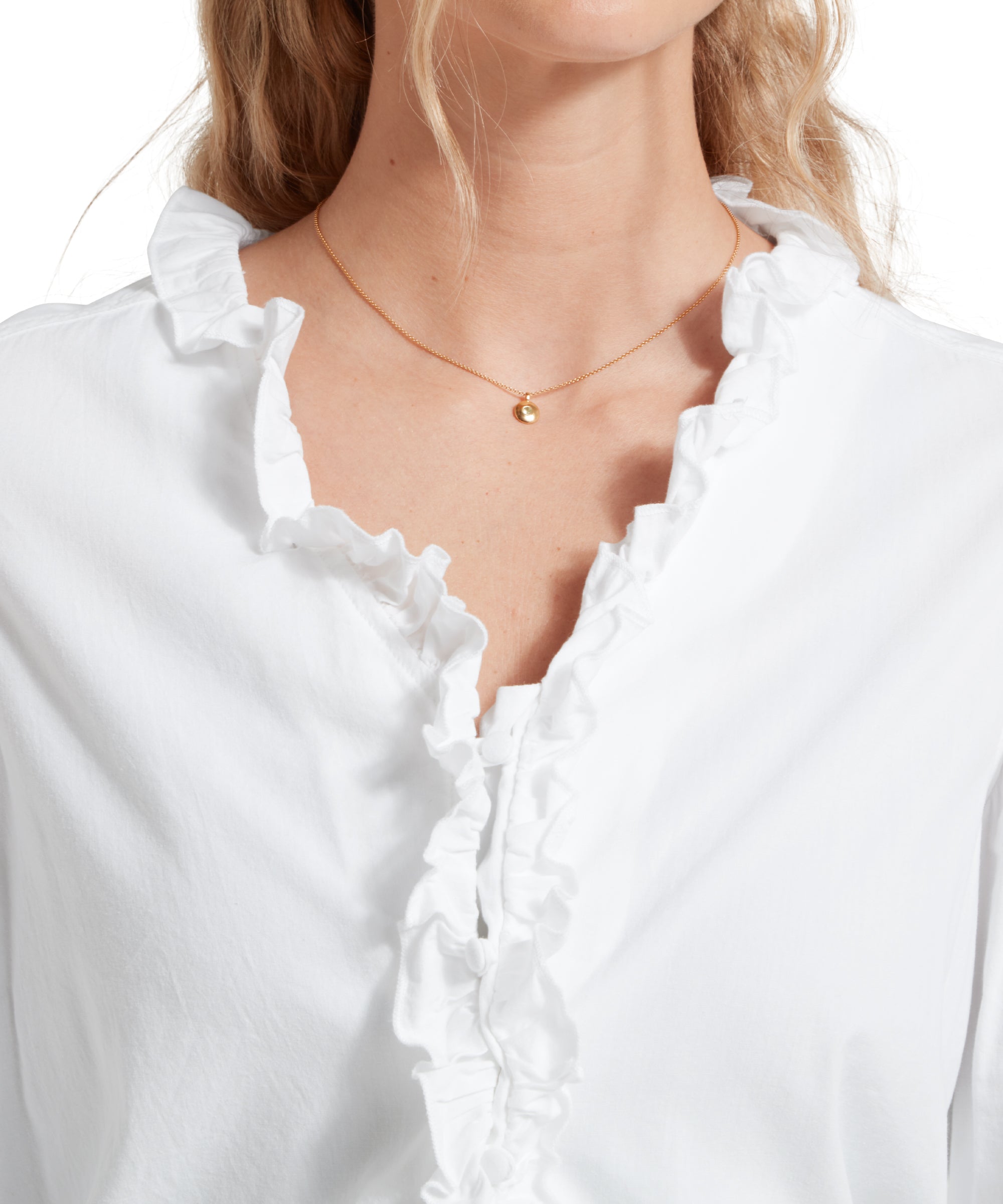 Close up image of a female model wearing a white Schöffel shirt, paired with gold accessories. Image highlights the ruffled collar.