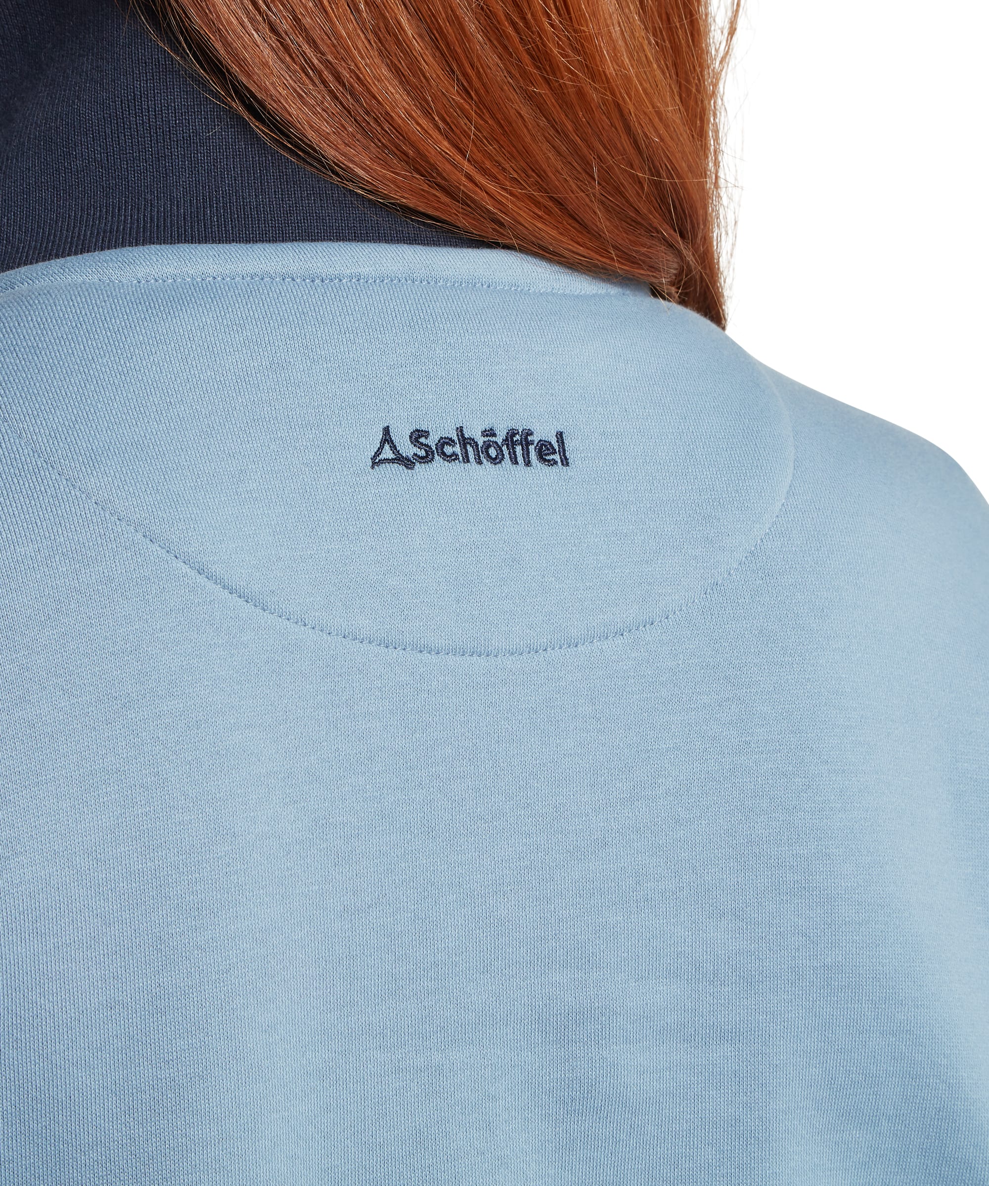 Close-up of the embroidered Schöffel logo at the back neck of the Women's Braunton 1/4 Zip Sweatshirt in Pale Blue, highlighting the tonal branding, raglan seam construction and contrast navy collar