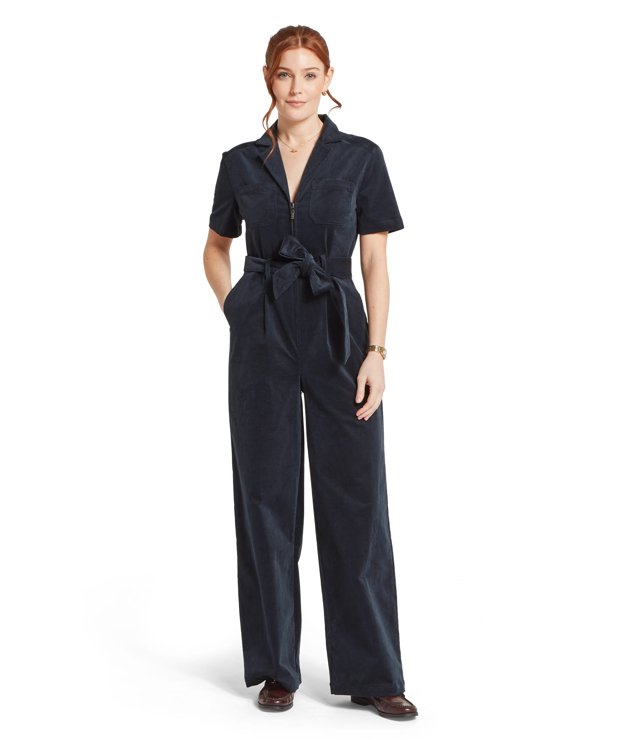 Schöffel Women's Briar Cord Jumpsuit in midnight navy, full-length front view showing wide-leg silhouette, short sleeves, V-neck with half zip, chest patch pockets and tie waist belt, styled with burgundy loafers