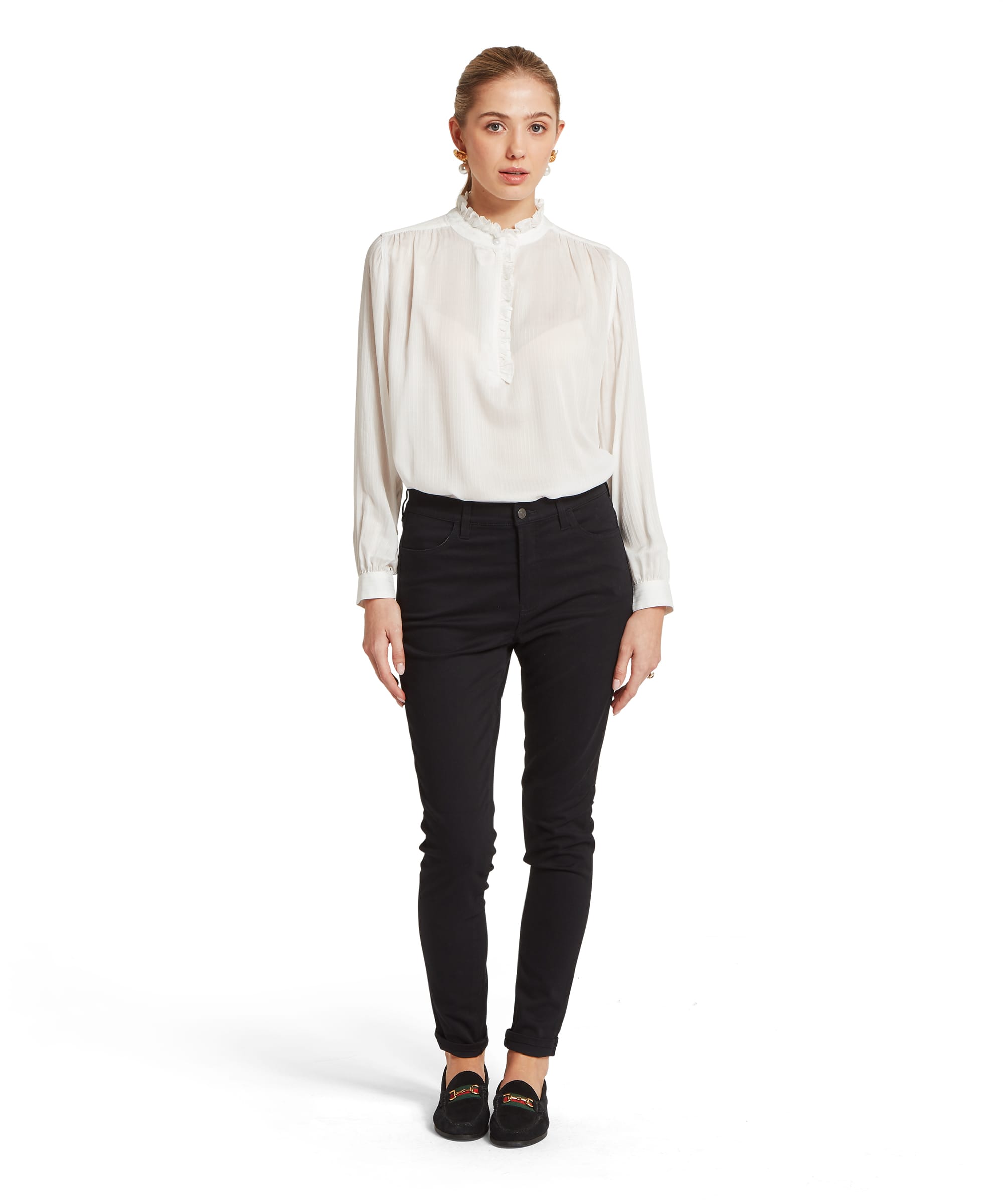 Full-length view of the Women's Schöffel Chelsworth Blouse in white, with its romantic frill-edged standing collar, ruched placket and voluminous sleeves with buttoned cuffs, tucked into slim black trousers with black velvet horsebit loafers.