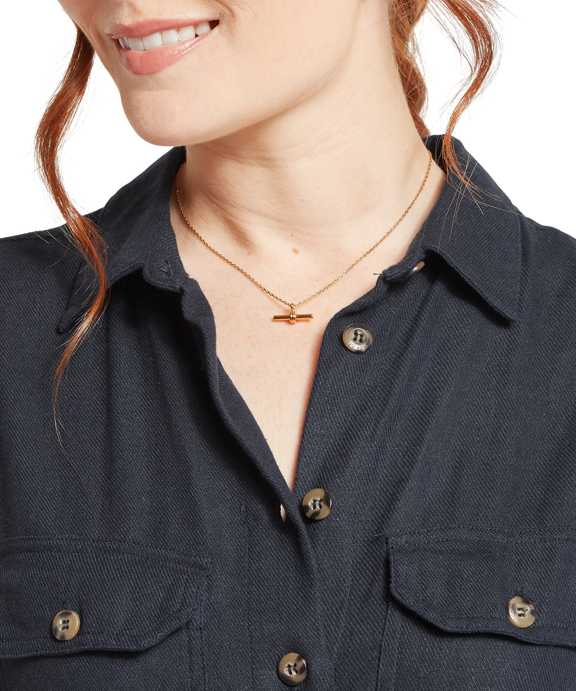 Close‑up of a woman wearing a navy textured button‑up shirt with two chest pockets, shown partially unbuttoned at the collar and styled with a delicate gold bar necklace.