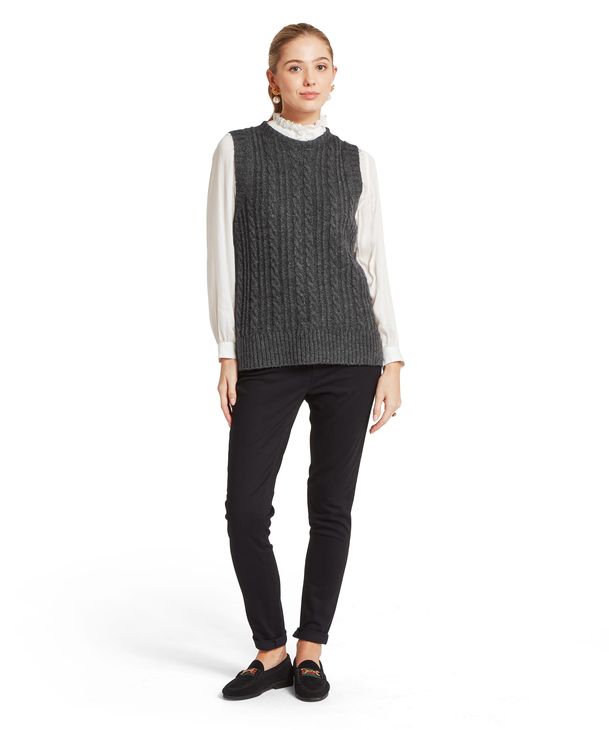 Schöffel Women's Evie Sleeveless Jumper in charcoal grey, full-length front view styled over a white ruffled-collar blouse with black slim trousers and black horsebit loafers, showing the cable-knit body, round neckline, and ribbed hem