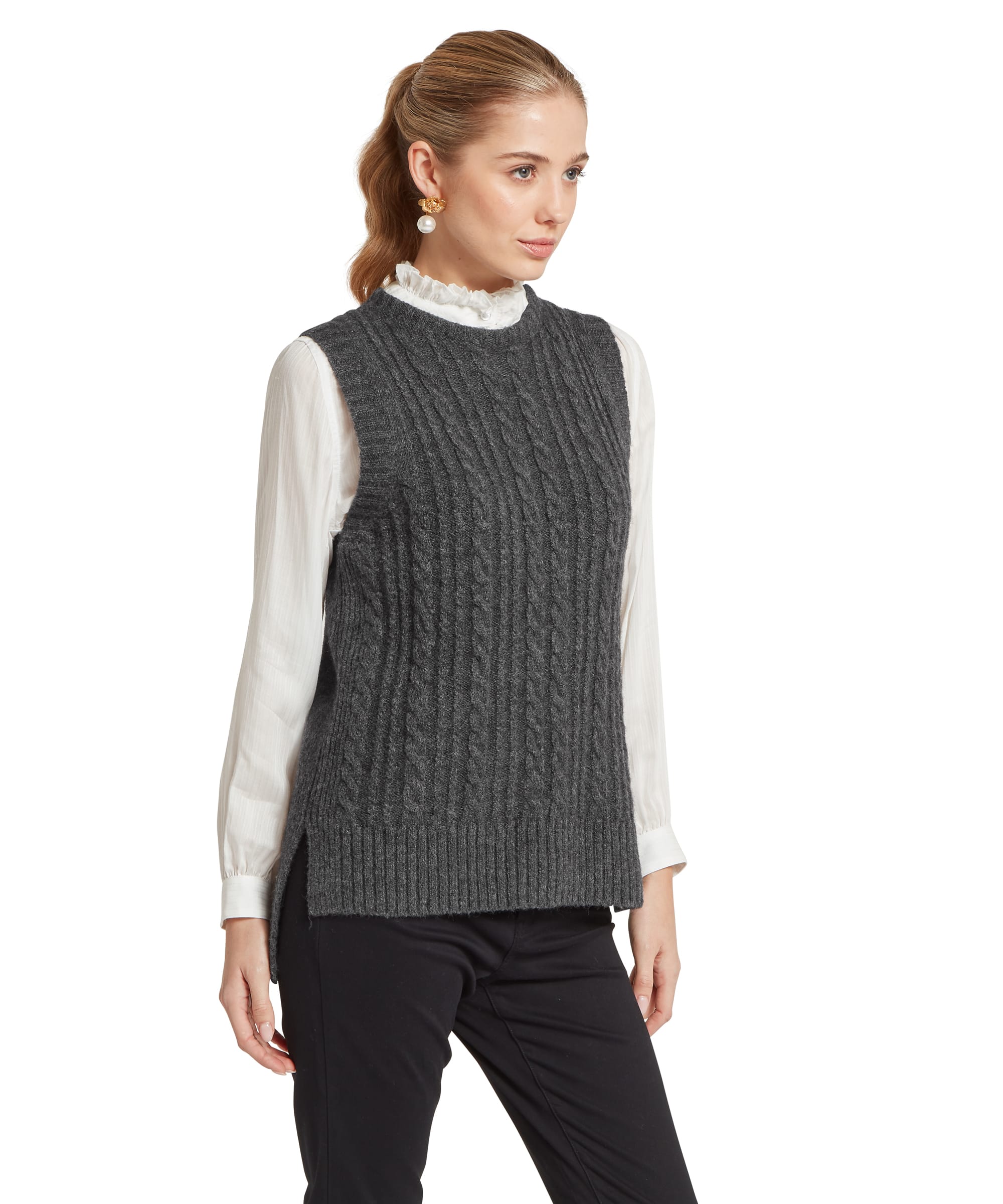Three-quarter view of a woman wearing the Schöffel Women's Evie Sleeveless Cable Knit Jumper in Charcoal, showing the textured cable-knit front panel and ribbed hem, layered over a white ruffled-collar shirt with black trousers