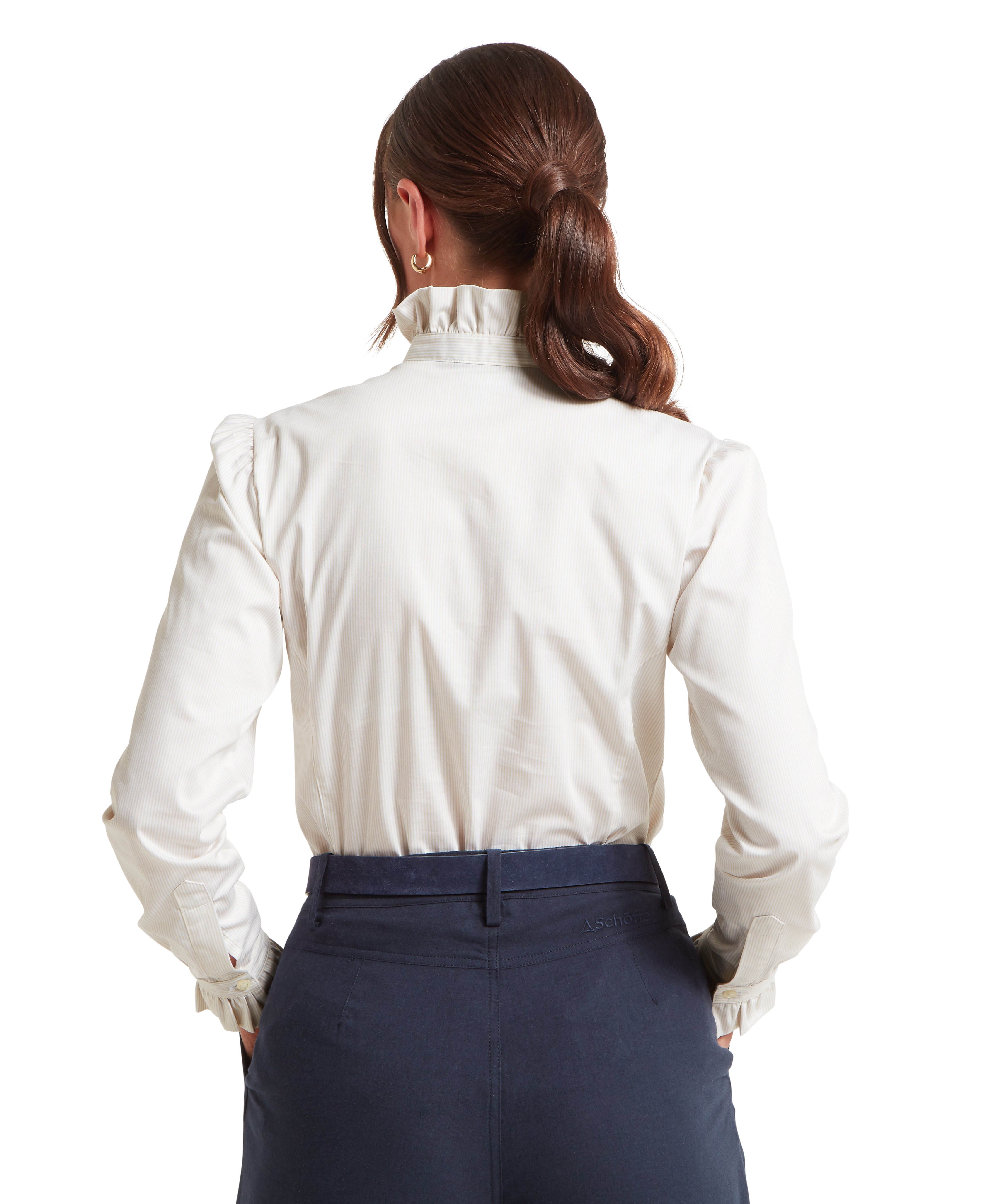 Woman seen from behind with her hair tied back in a low ponytail, wearing a white long-sleeved blouse with delicate ruffles around the high collar and cuffs. The blouse features thin vertical stripes and a subtle gathered detail at the shoulders, and it is tucked into a pair of high-waisted navy blue trousers. She has both hands tucked into her back pockets, showcasing the clean, tailored fit of the ensemble.