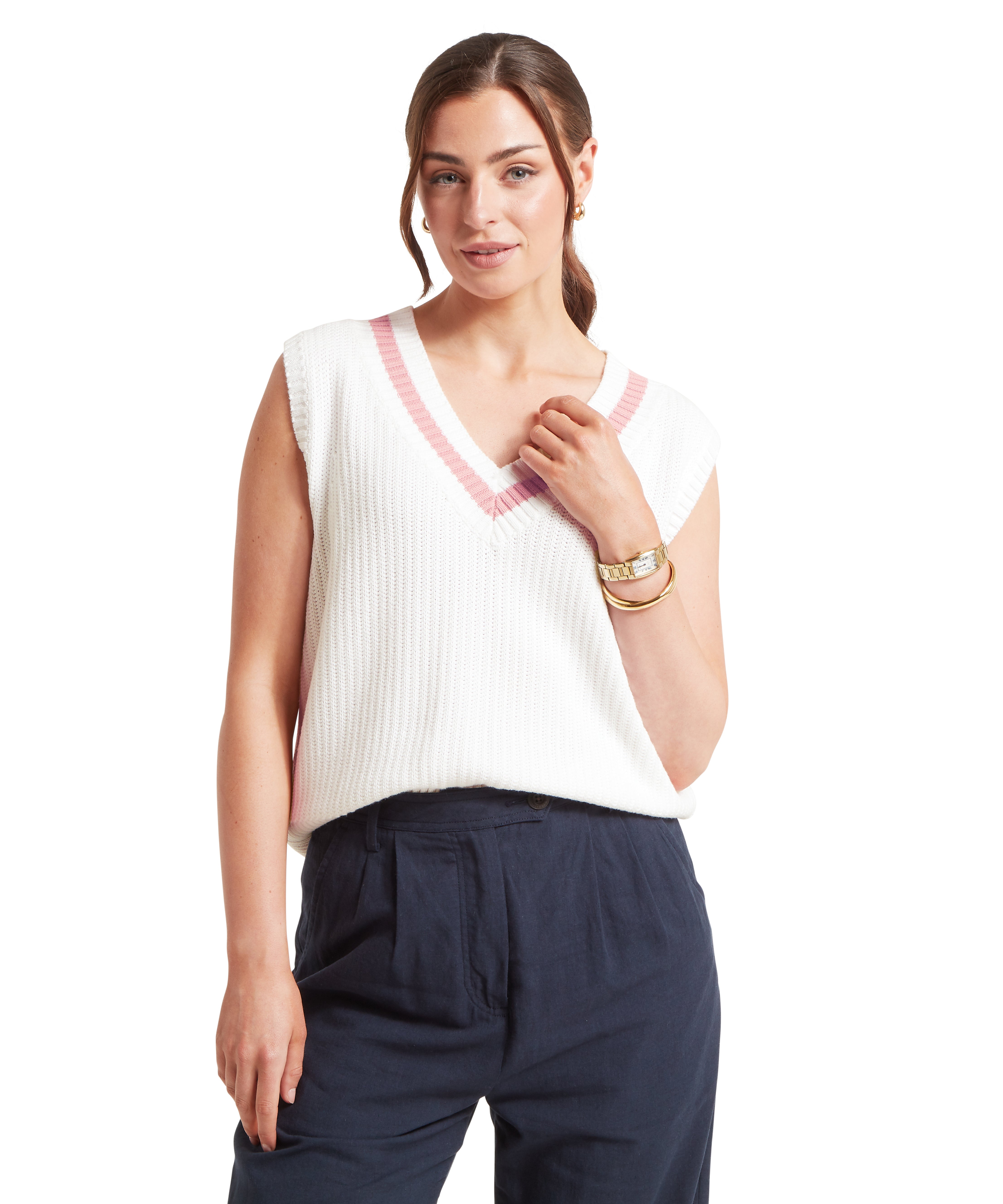 Woman wearing a white knitted vest with a V-neckline featuring a pink trim. Paired with high-waisted, pleated navy trousers with side pockets. Styled with gold bracelets and a watch on the left wrist. Standing front-facing against a plain white background.
