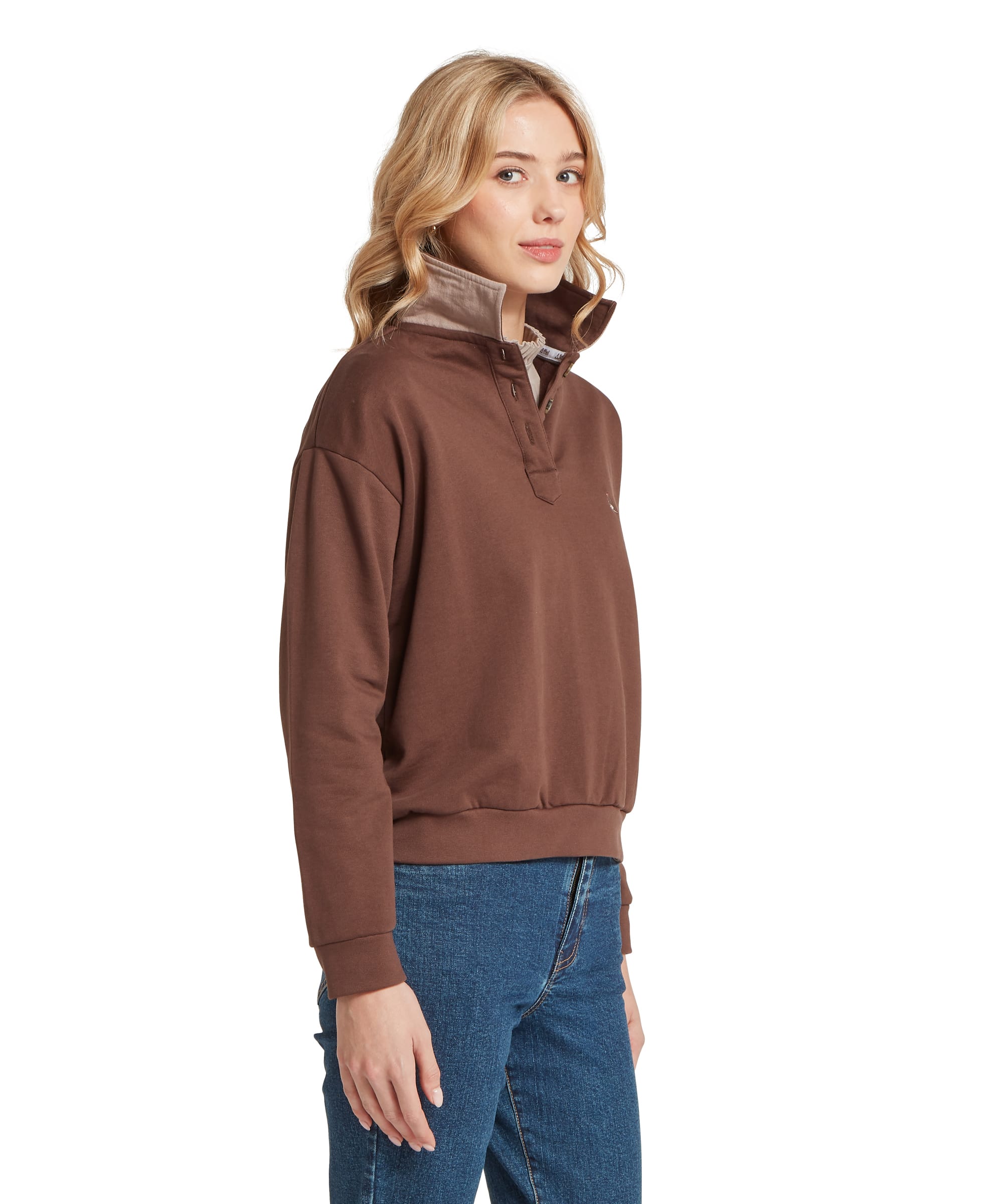 Three-quarter view of a woman wearing the Schöffel Women's Horseley Rugby Sweatshirt in Chocolate Brown, featuring the contrast camel storm collar, snap-button placket and embroidered Schöffel guinea fowl logo, layered over a cream polo neck top and blue jeans