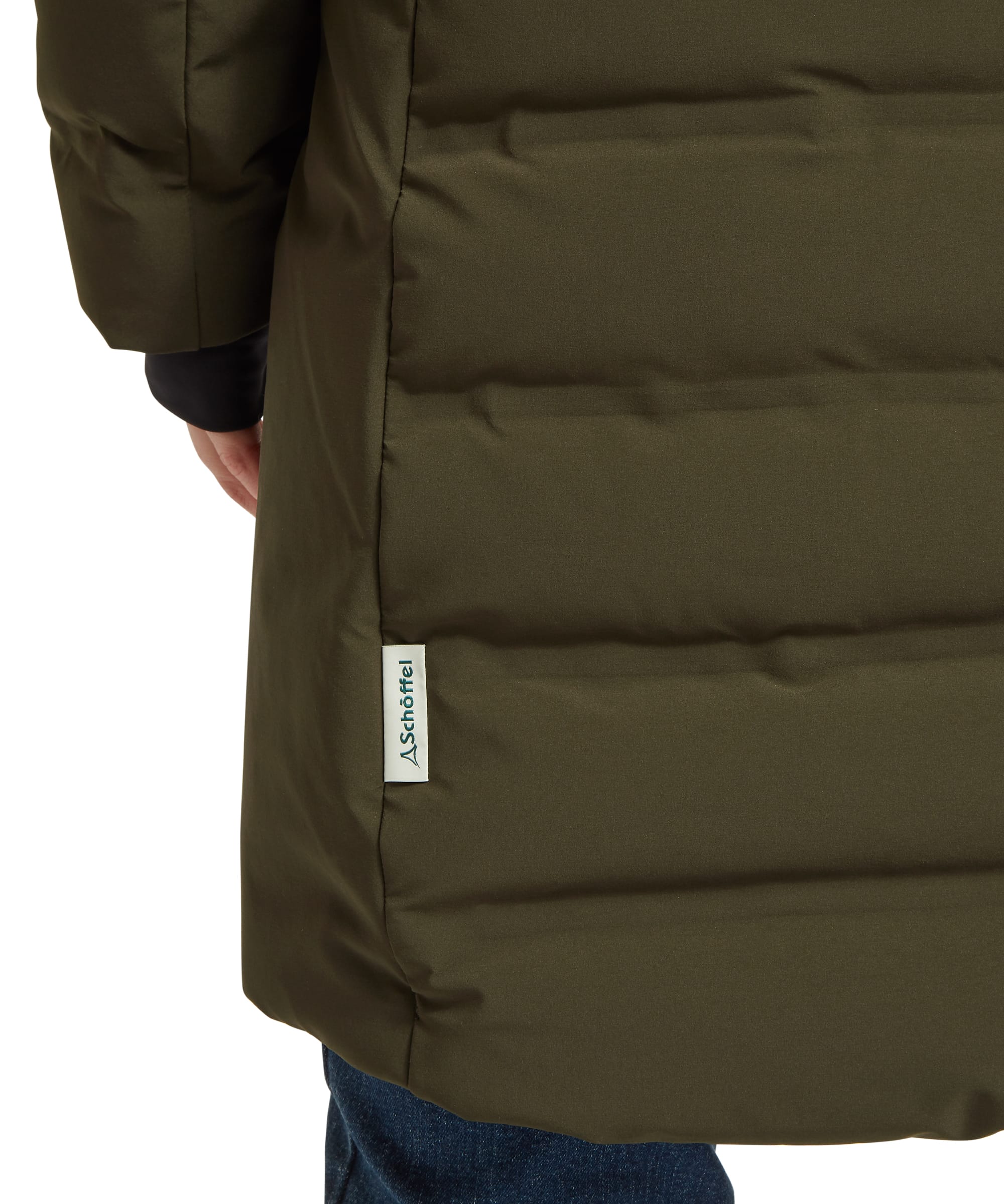 Side hem detail of the Schöffel Women's Hurlingham Waterproof Down Coat in olive green, showing the quilted baffles, knitted inner cuff, and Schöffel branded label at the lower side seam