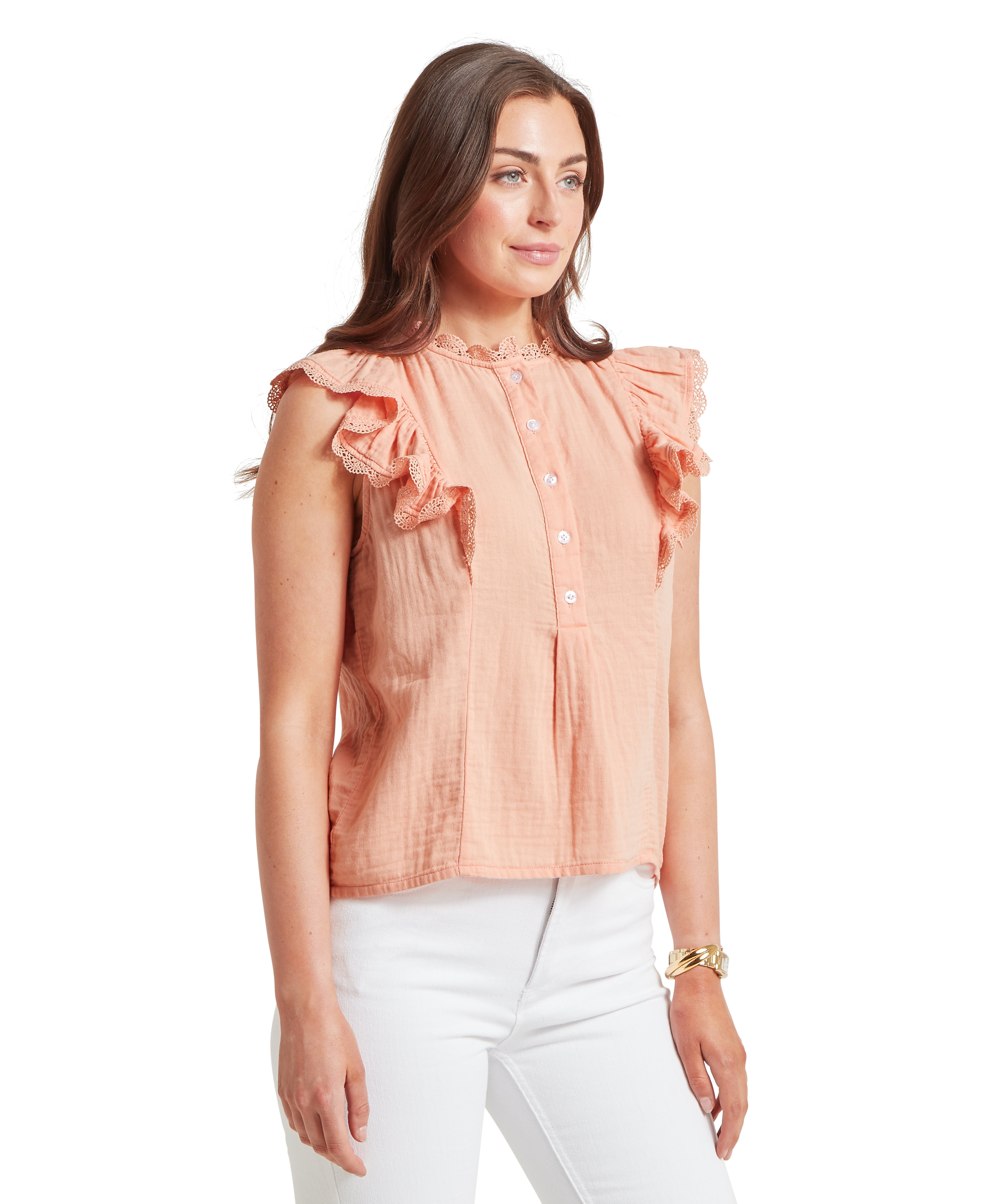 Woman wearing a sleeveless peach‑coloured blouse with ruffled lace‑trimmed shoulders and a front button‑through placket. The textured fabric has a relaxed fit and is paired with white trousers. Displayed against a plain white background.