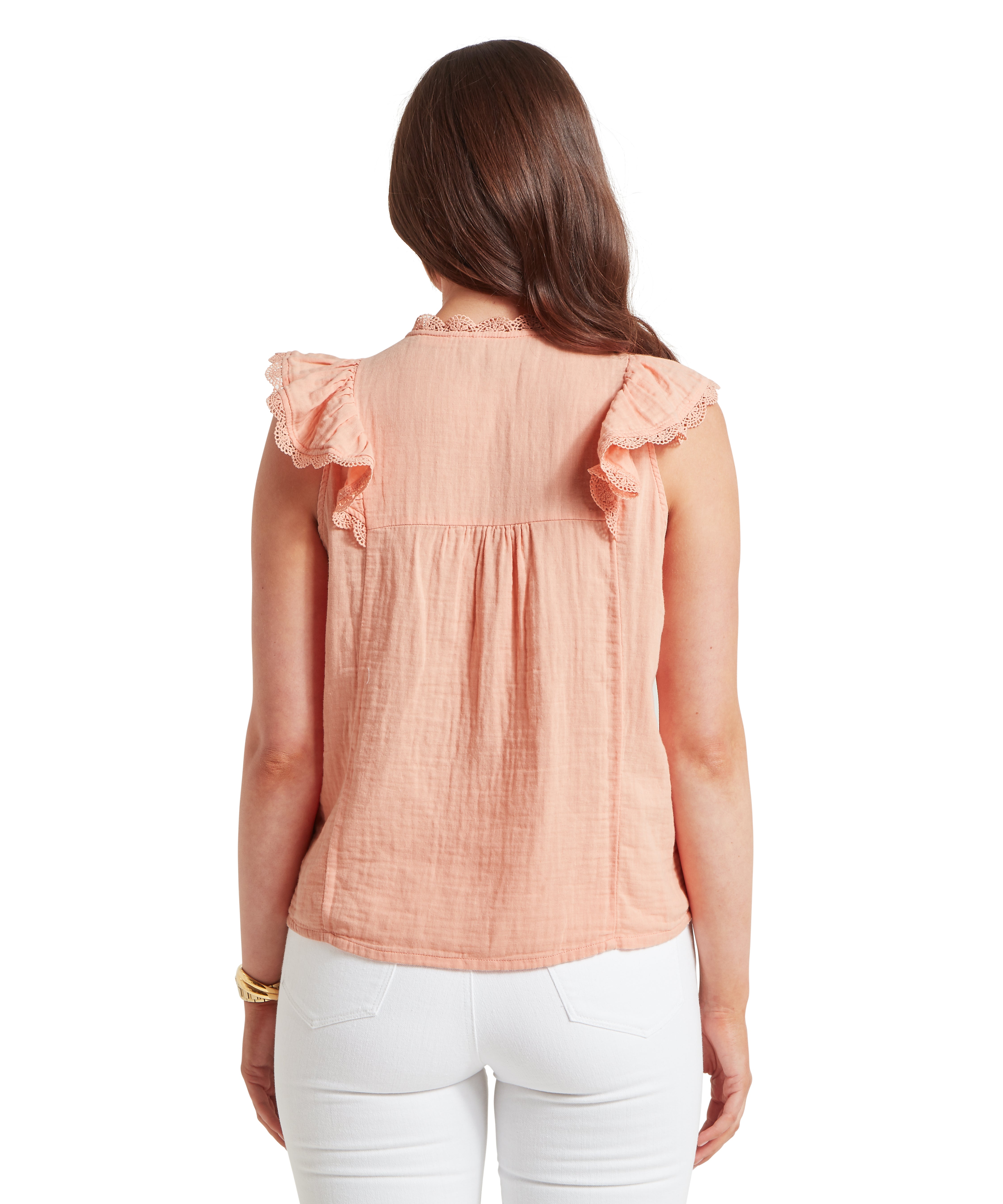Back view of a woman wearing a sleeveless peach-coloured blouse with ruffled sleeves and delicate lace trim. The blouse features a gathered detail below the neckline and is paired with white trousers. She has long, straight brown hair and wears a gold bracelet on her left wrist. Displayed against a plain white background.