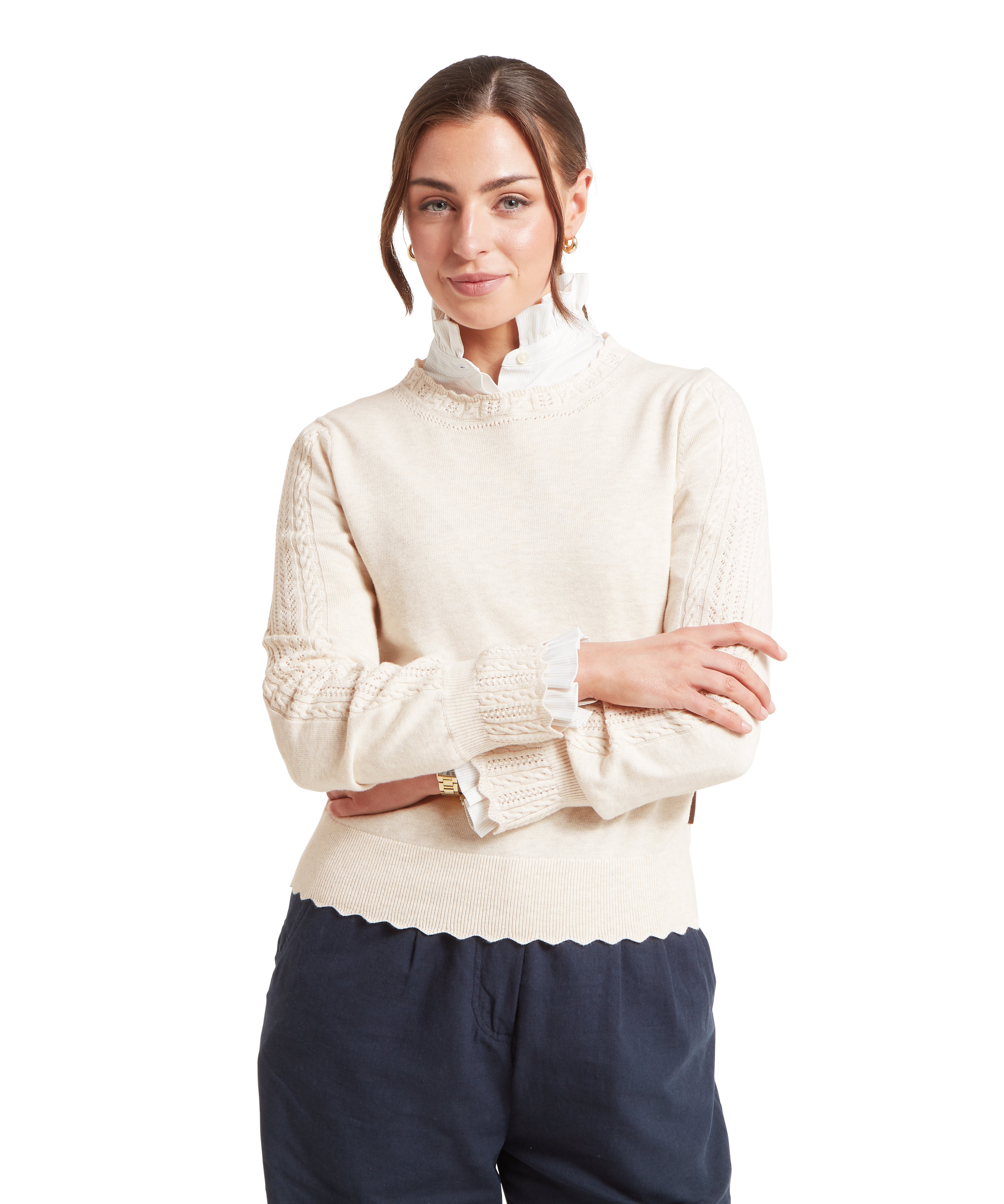Woman wearing a cream sweater and navy trousers against a white background