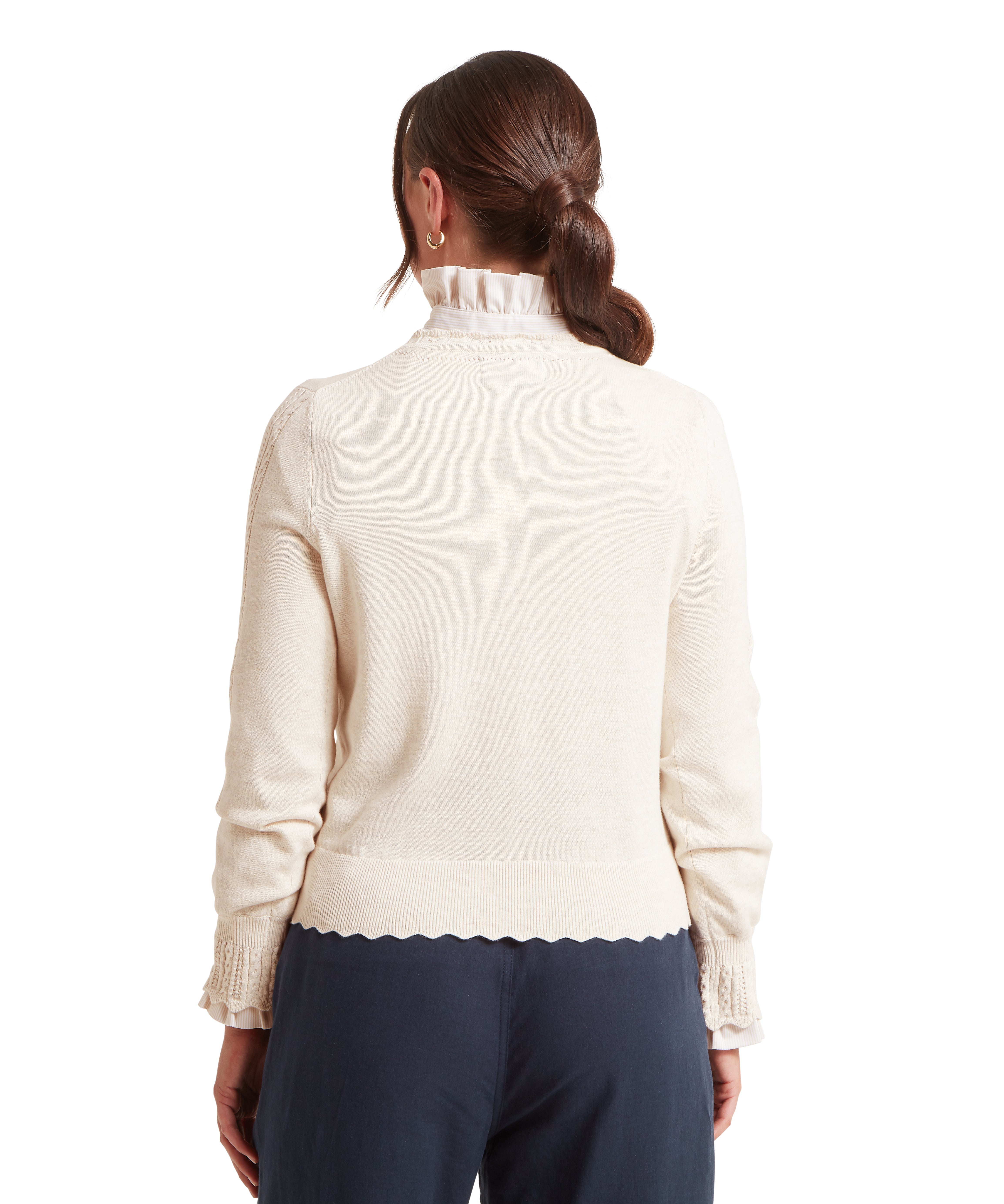 Back view of a woman wearing a cream coloured long-sleeve knitted jumper with a ribbed hem and cuffs. Paired with dark blue pants and a white shirt, the woman has dark brown hair styled in a low ponytail and is posed against a plain white background.