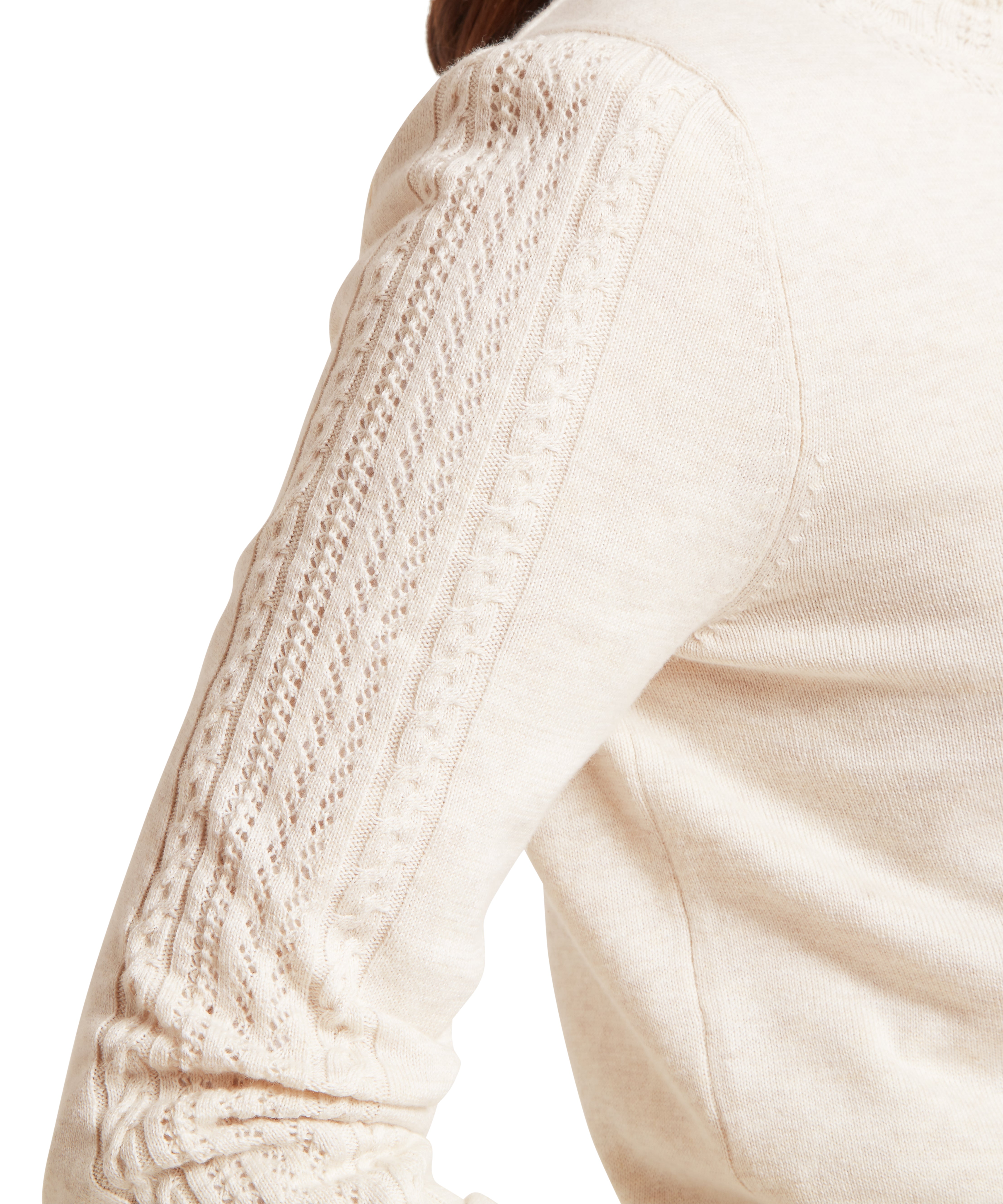 Close-up of a person’s right arm and shoulder wearing a beige knitted jumper with intricate sleeve detailing. The sleeve features vertical rows of openwork lace and cable knit patterns, showcasing texture and craftsmanship. The soft material and refined design are highlighted against a plain white background.