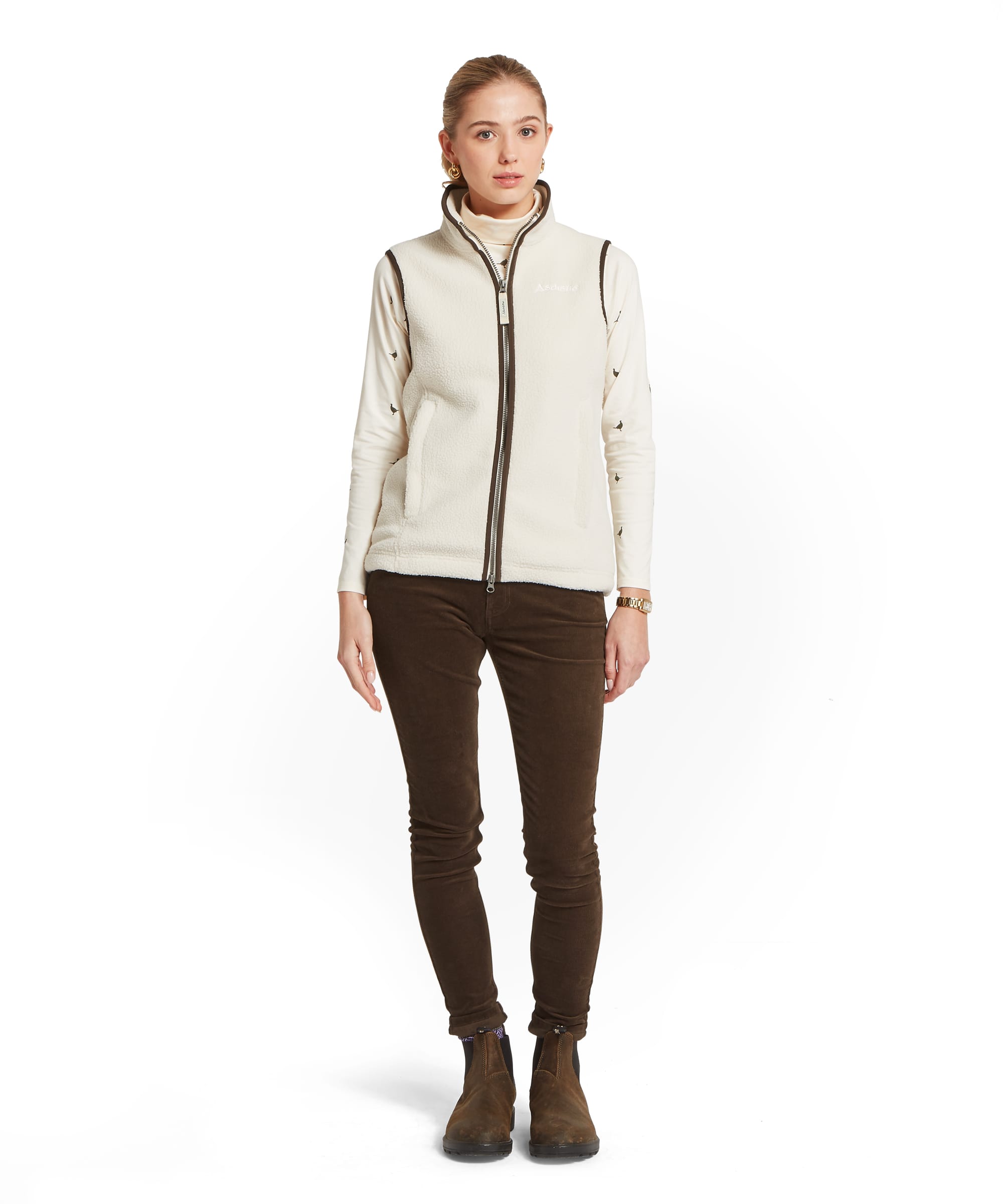 Full-length view of the Women's Schöffel Lyndon Retro Fleece Gilet in ecru white sherpa fleece with dark brown contrast detailing, layered over the pheasant print Malham Top, with dark olive cord trousers and suede Chelsea boots.