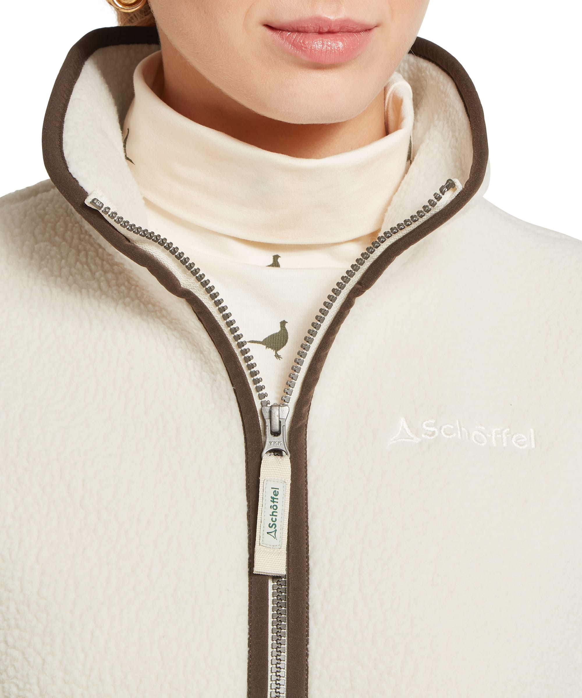 Schöffel Women's Lyndon Retro Fleece Gilet in Cream — close-up of full-zip fastening, dark khaki binding and embroidered Schöffel logo, layered over pheasant-print base layer