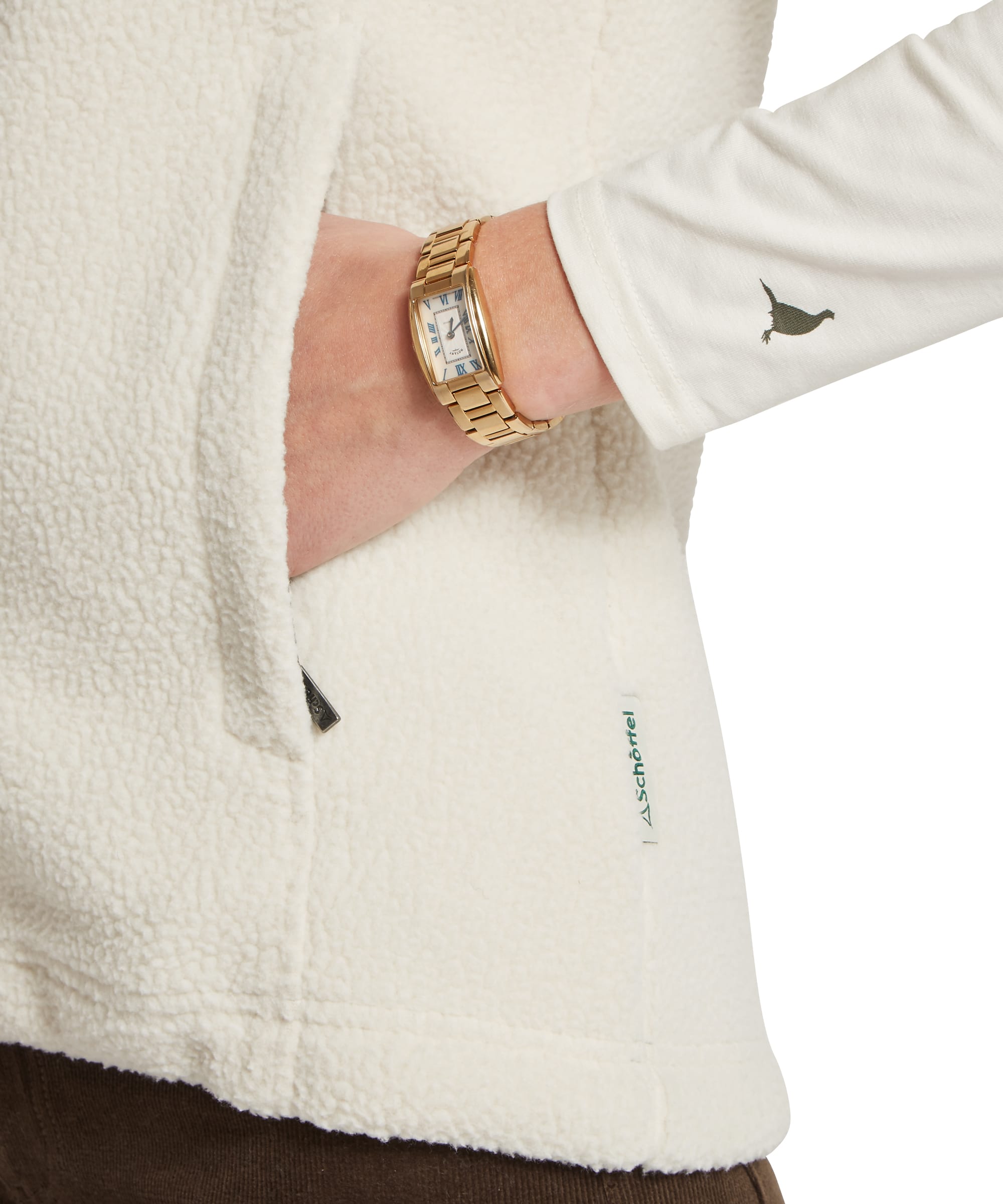 Side pocket detail of the Schöffel Women's Lyndon Retro Fleece Gilet in cream white, showing the deep hand-warmer pocket in chunky sherpa-style fleece, Schöffel woven label, and embroidered pheasant motif on the sleeve of the white base layer worn beneath