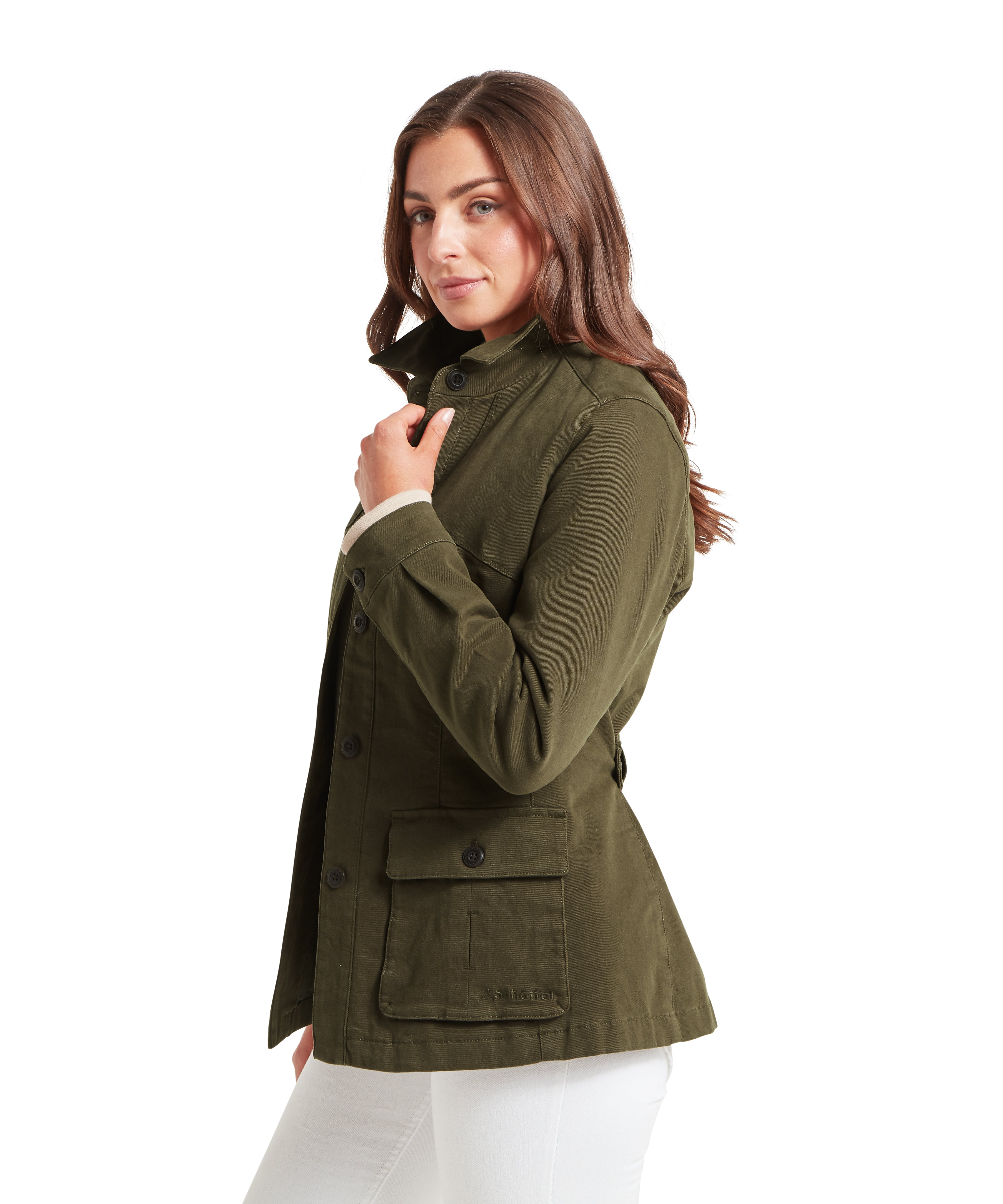 Woman posing in profile view, wearing an olive green button-up jacket with a high collar and flap pockets, paired with white pants. The jacket has a textured fabric and tailored fit, with buttons down the front and on the pockets. The individual is holding one hand near the collar, emphasizing the garment’s design and fit, against a plain white background.