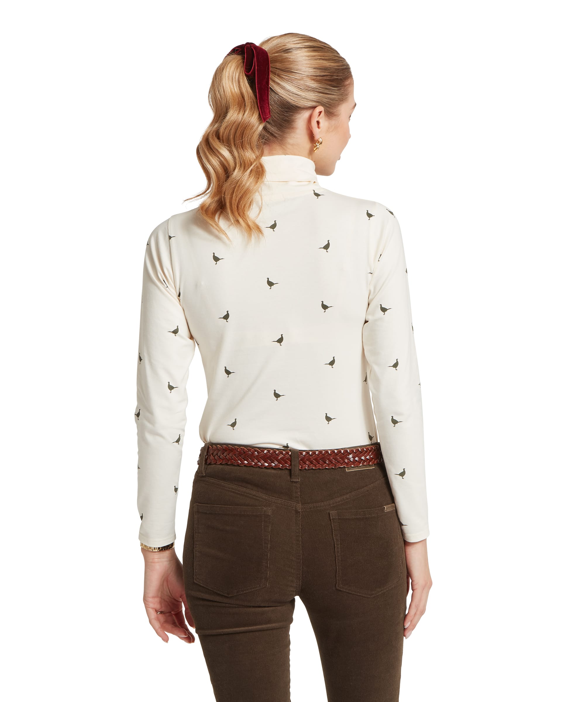 Rear view of the Women's Schöffel Malham Top in sage green pheasant print on cream, showing the all-over scattered bird print across the fitted roll neck and long-sleeve silhouette, styled with dark olive cord trousers and a tan plaited belt.