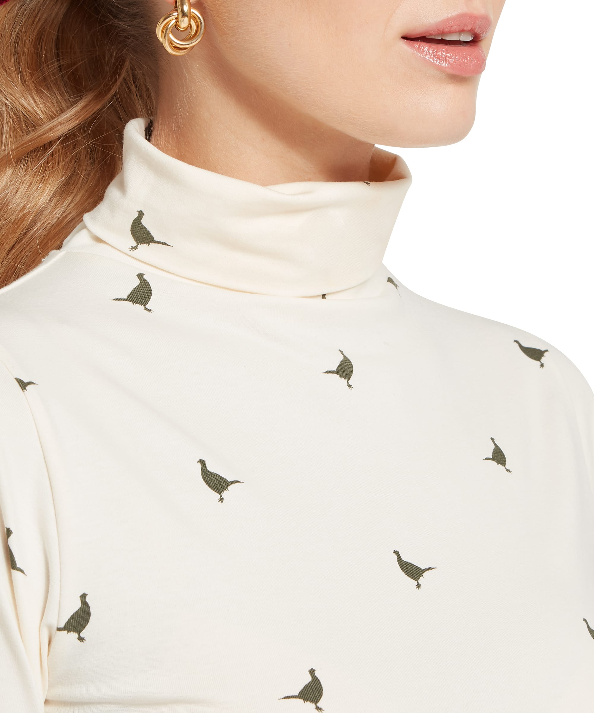 Close-up detail of the Women's Schöffel Malham Top in sage green pheasant print on cream, showing the tonal grouse motif and the snug roll neck, with a gold hoop earring visible.