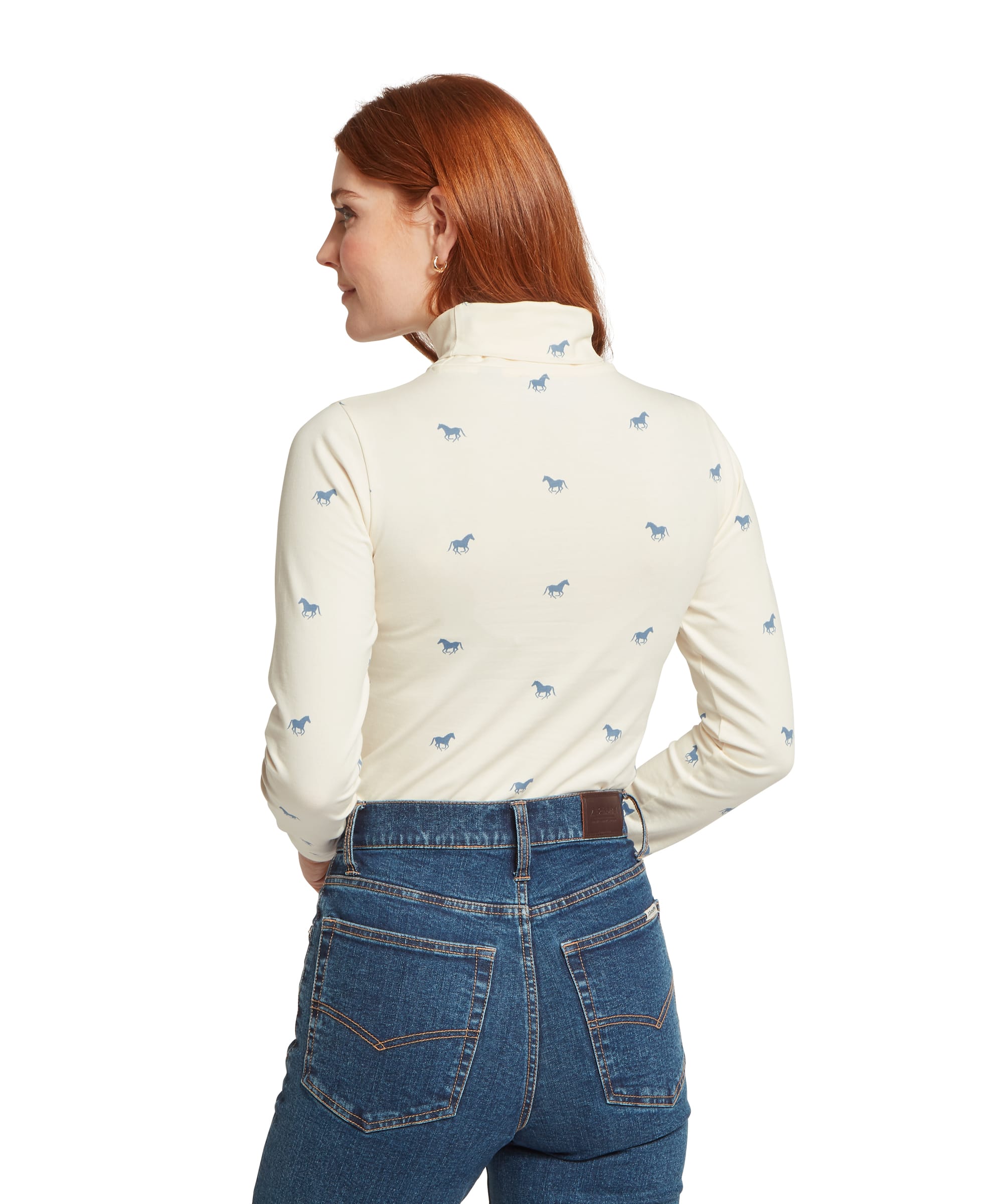 Rear view of the Women's Schöffel Malham Top in blue horse print on cream, highlighting the all-over scattered running horse motif and close-fit roll neck silhouette, worn with blue denim jeans.
