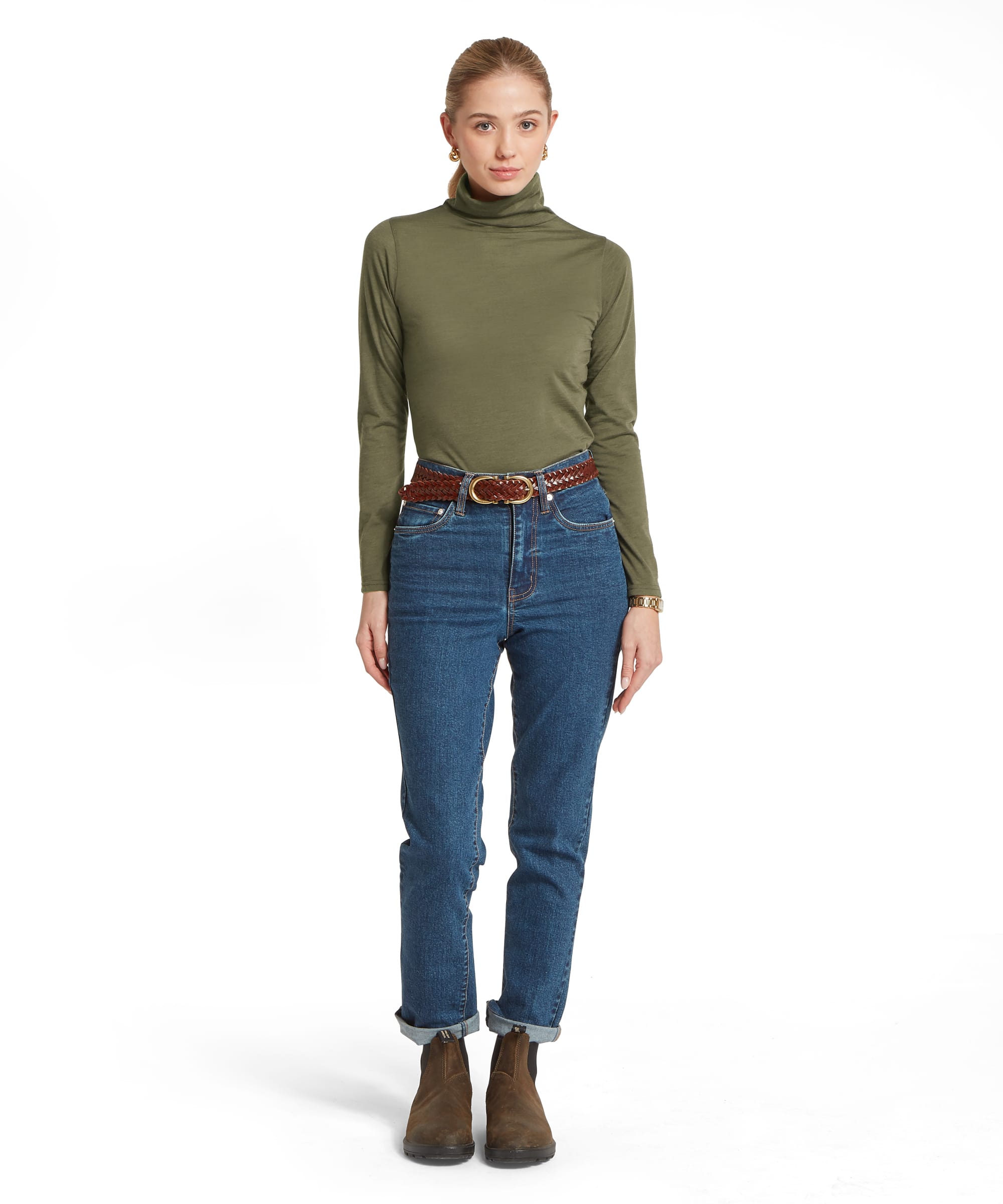 Full-length front view of the Schöffel Women's Malton Merino Roll Neck Top in Khaki Green, styled with straight-leg blue jeans, a tan belt and suede ankle boots for a classic country look