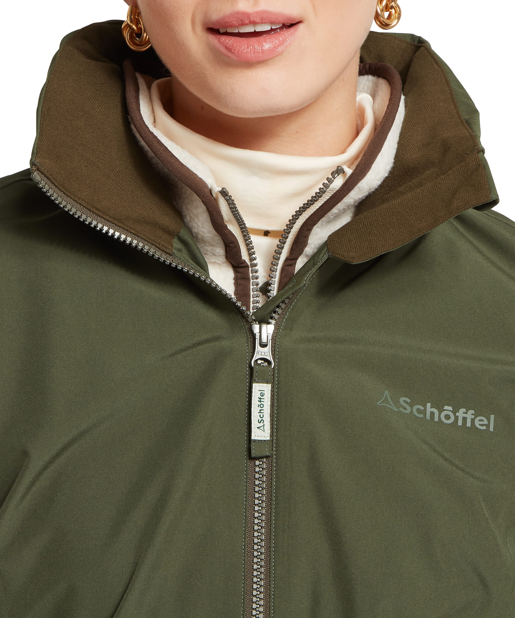 Close-up of the storm collar and Schöffel branded zip on the Women's Manton Lightweight Waterproof Jacket in Dark Olive, showing the contrast fleece inner collar lining and layering over a cream roll neck top