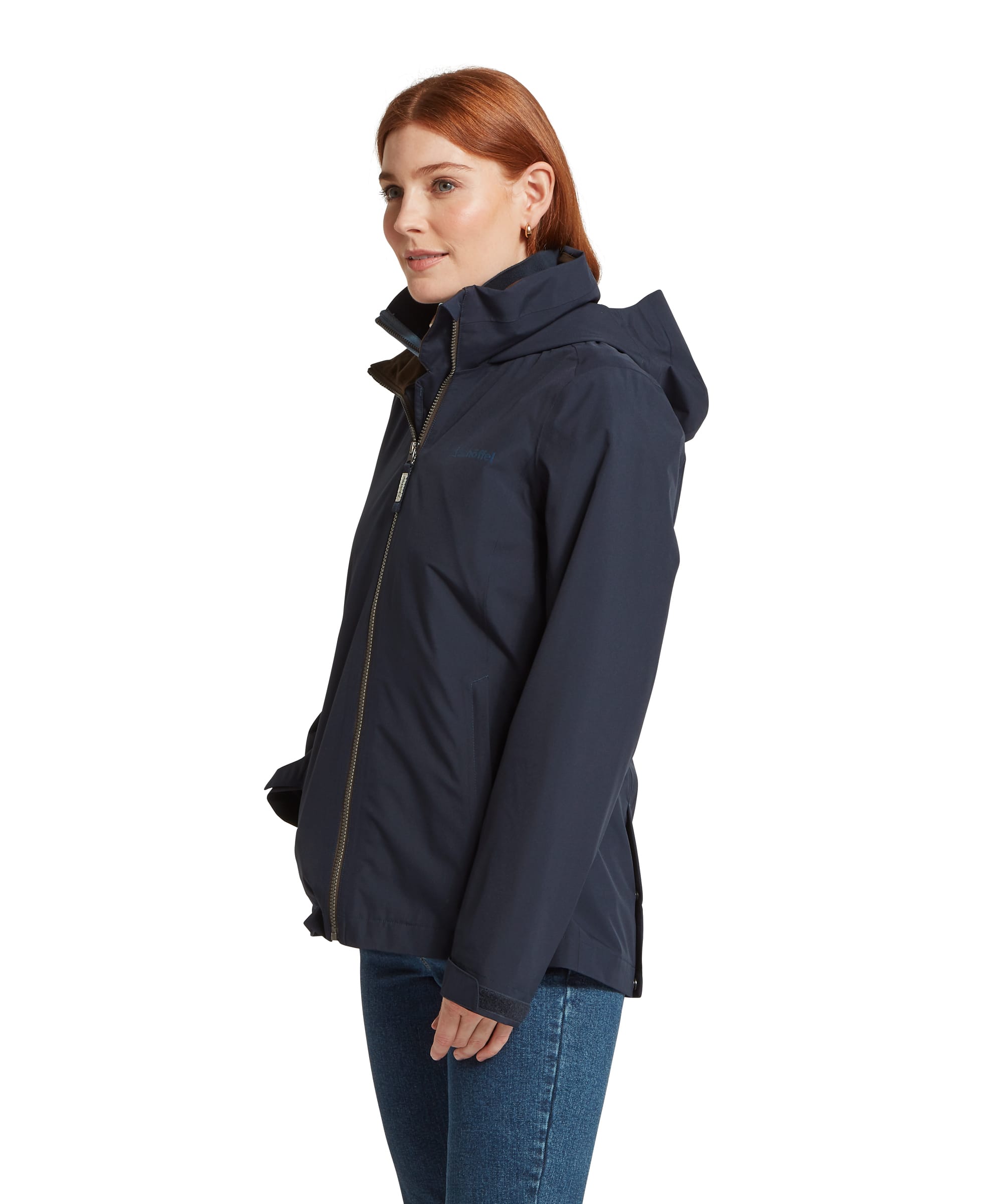 Side view of the Women's Schöffel Manton Lightweight Waterproof Jacket in midnight navy, featuring a zip-away hood, antique brass full-length zip, Schöffel chest logo and inner gaiter cuffs, paired with blue denim jeans.
