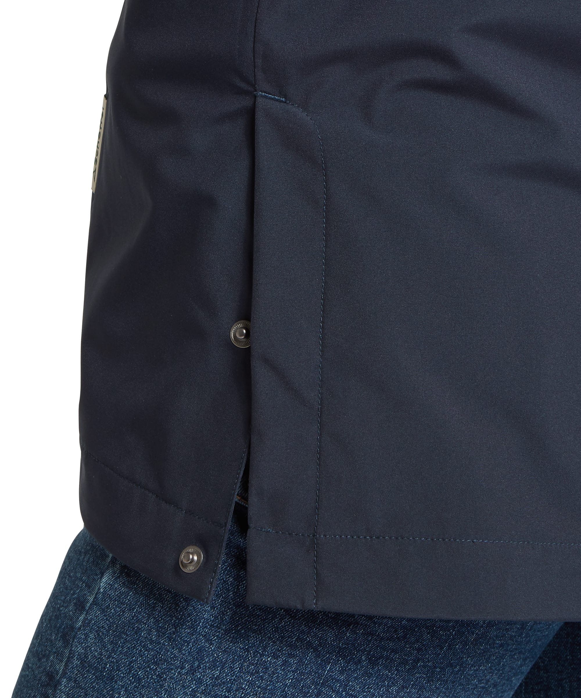 Close-up hem and cuff detail of the Schöffel Women's Manton Lightweight Waterproof Jacket in navy, showing the herringbone fabric texture, adjustable press-stud cuff tab, clean hemline stitching and side seam, worn with blue jeans