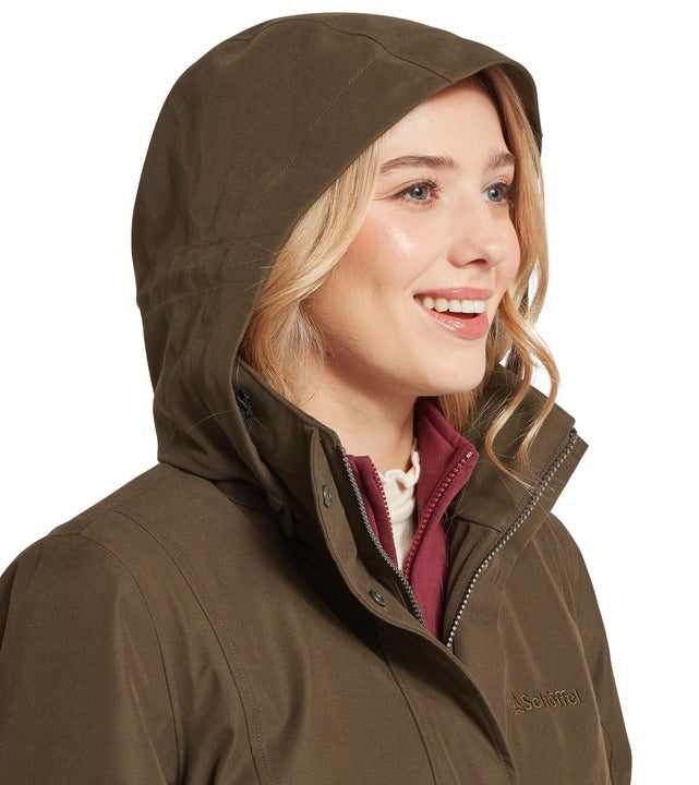 Schöffel Marefield waterproof coat in green, close-up of woman wearing hood up with contrast burgundy collar and embroidered logo