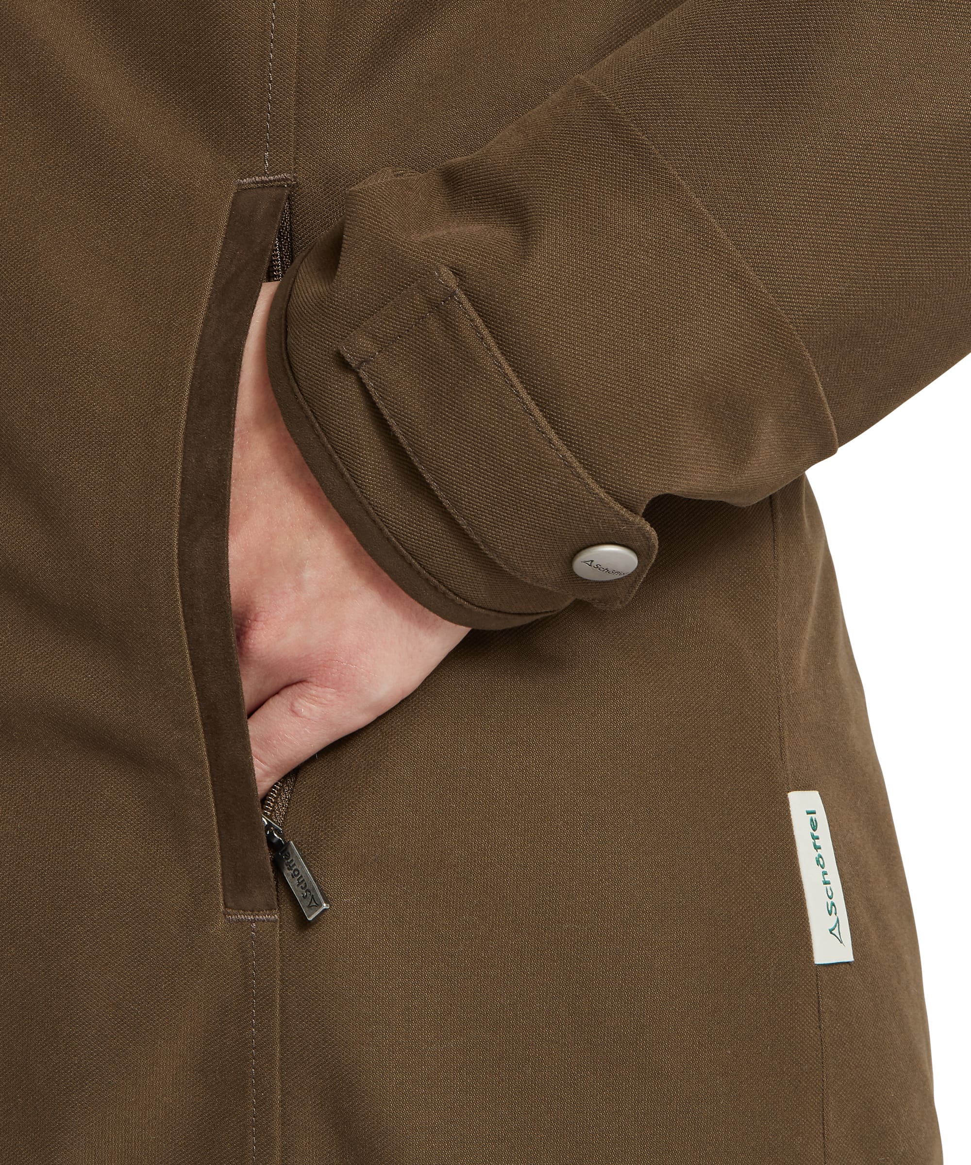 Close-up detail of the Women's Schöffel Marefield Waterproof Coat in dark khaki green, showing the hand in the zip side pocket, the suede-effect elbow patch, adjustable cuff tab with Schöffel press stud and branded woven label.