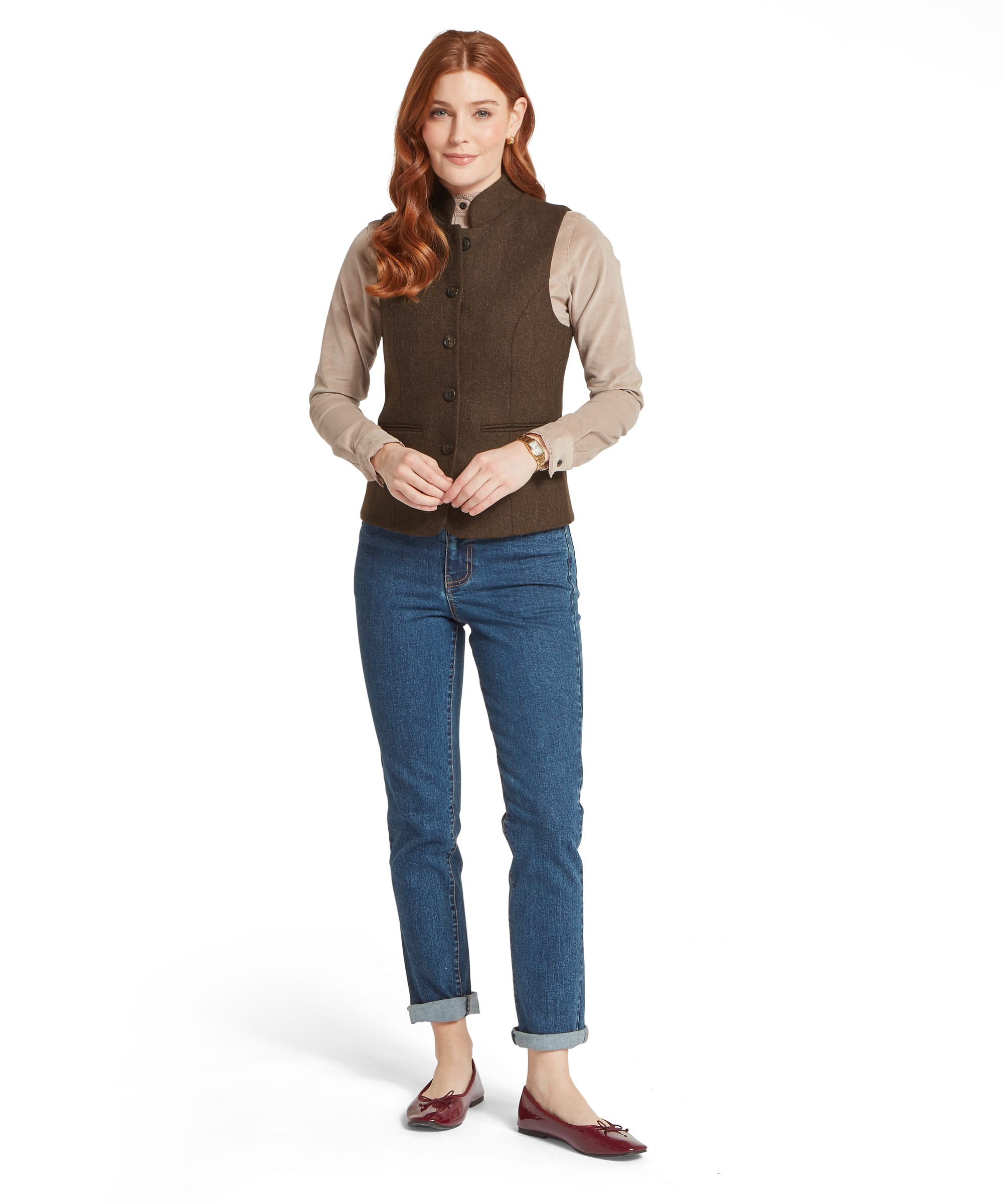 Full-length view of the Women's Schöffel Millport Tweed Nehru Waistcoat in dark brown herringbone, styled over a camel cord shirt, with relaxed-fit blue denim jeans with turn-ups and burgundy patent ballet flats.