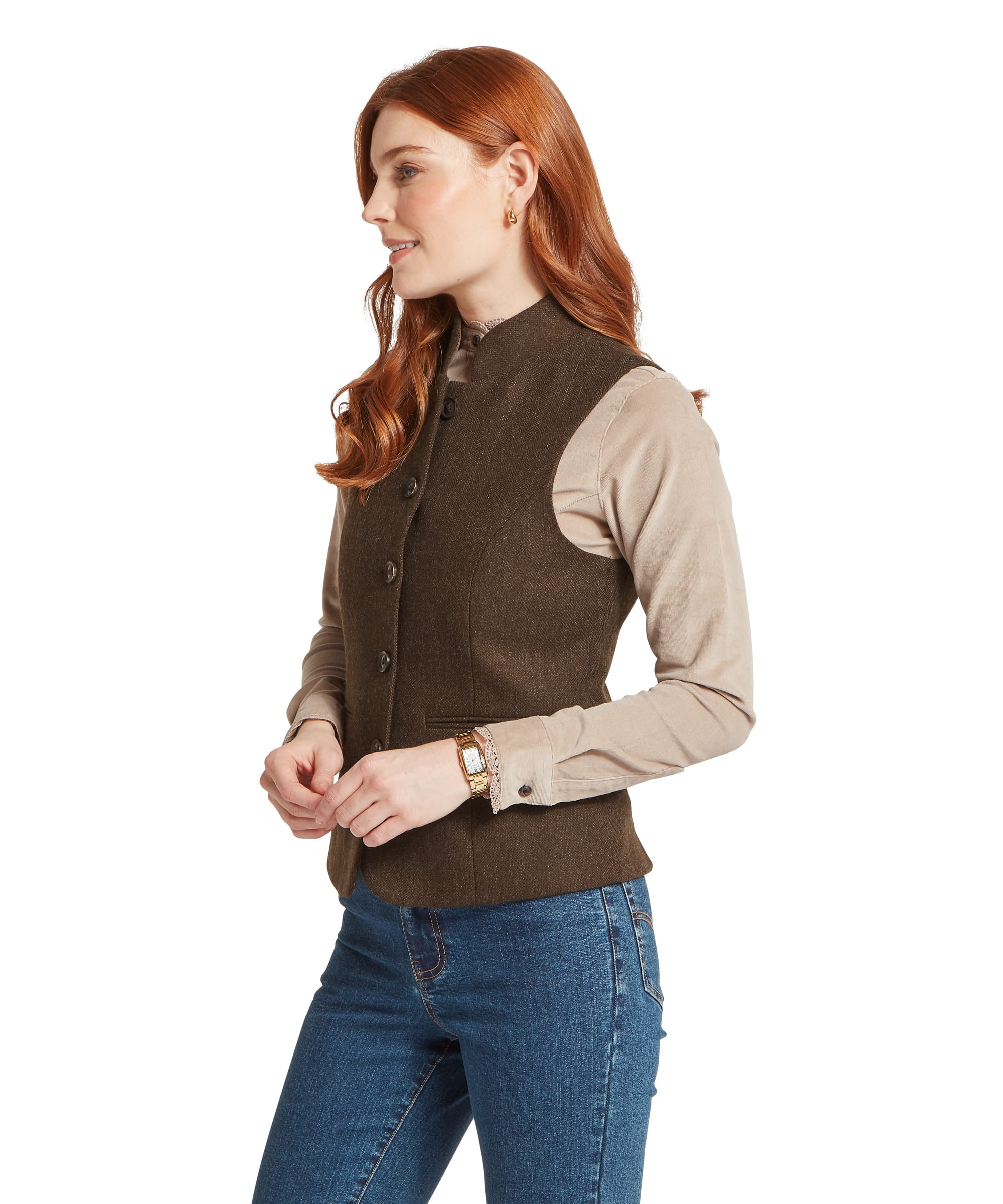 Side view of the Women's Schöffel Millport Tweed Nehru Waistcoat in dark brown herringbone tweed, showing the fitted waist seaming, welt pocket and button fastening, worn over a camel cord shirt with blue jeans and a gold watch.