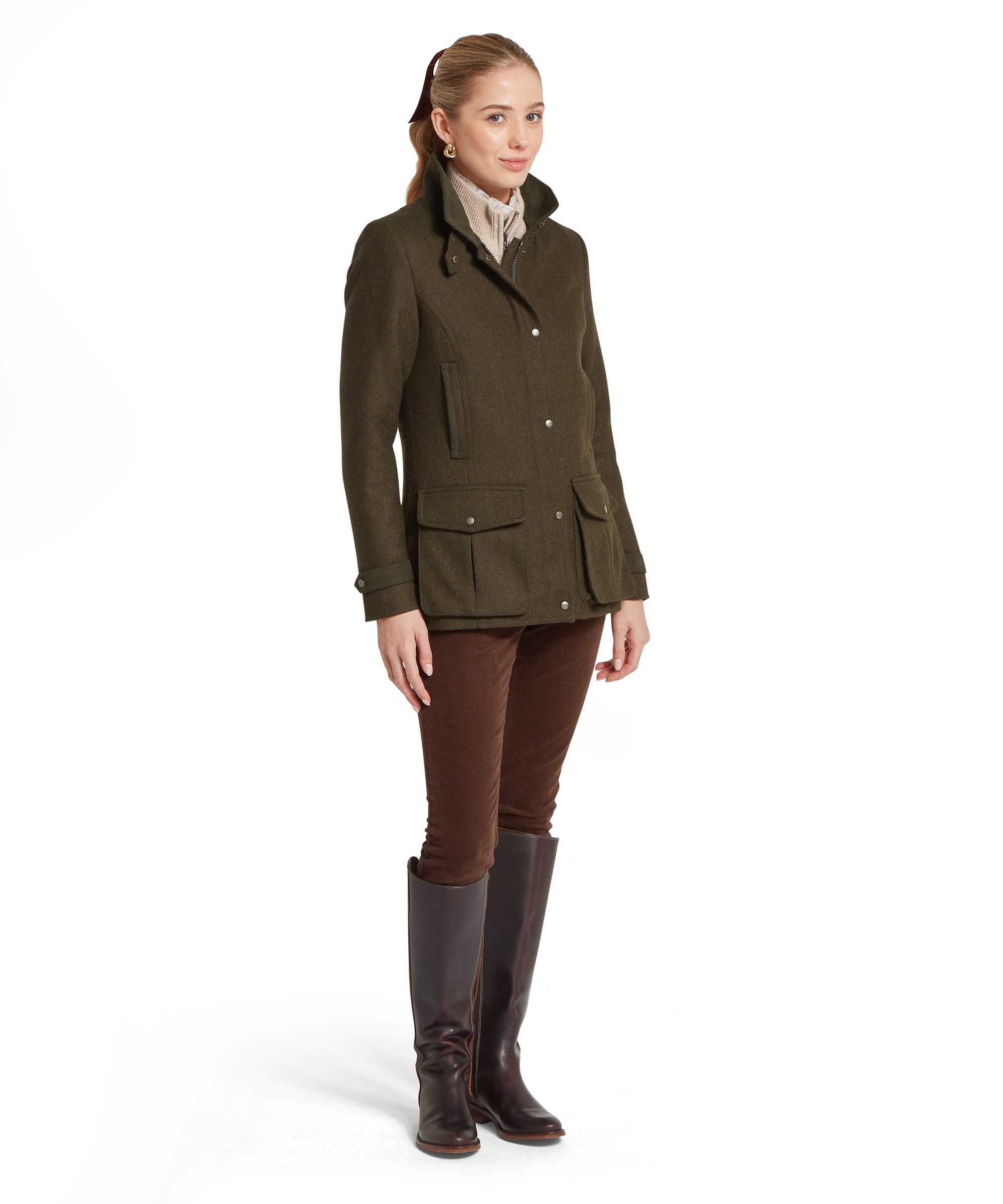 Schöffel Women's Murra Tweed Coat in dark olive herringbone tweed, three-quarter front view showing snap-button and zip fastening, flap patch pockets, suede collar trim and stand collar, styled with brown cord trousers and dark leather knee-high boots