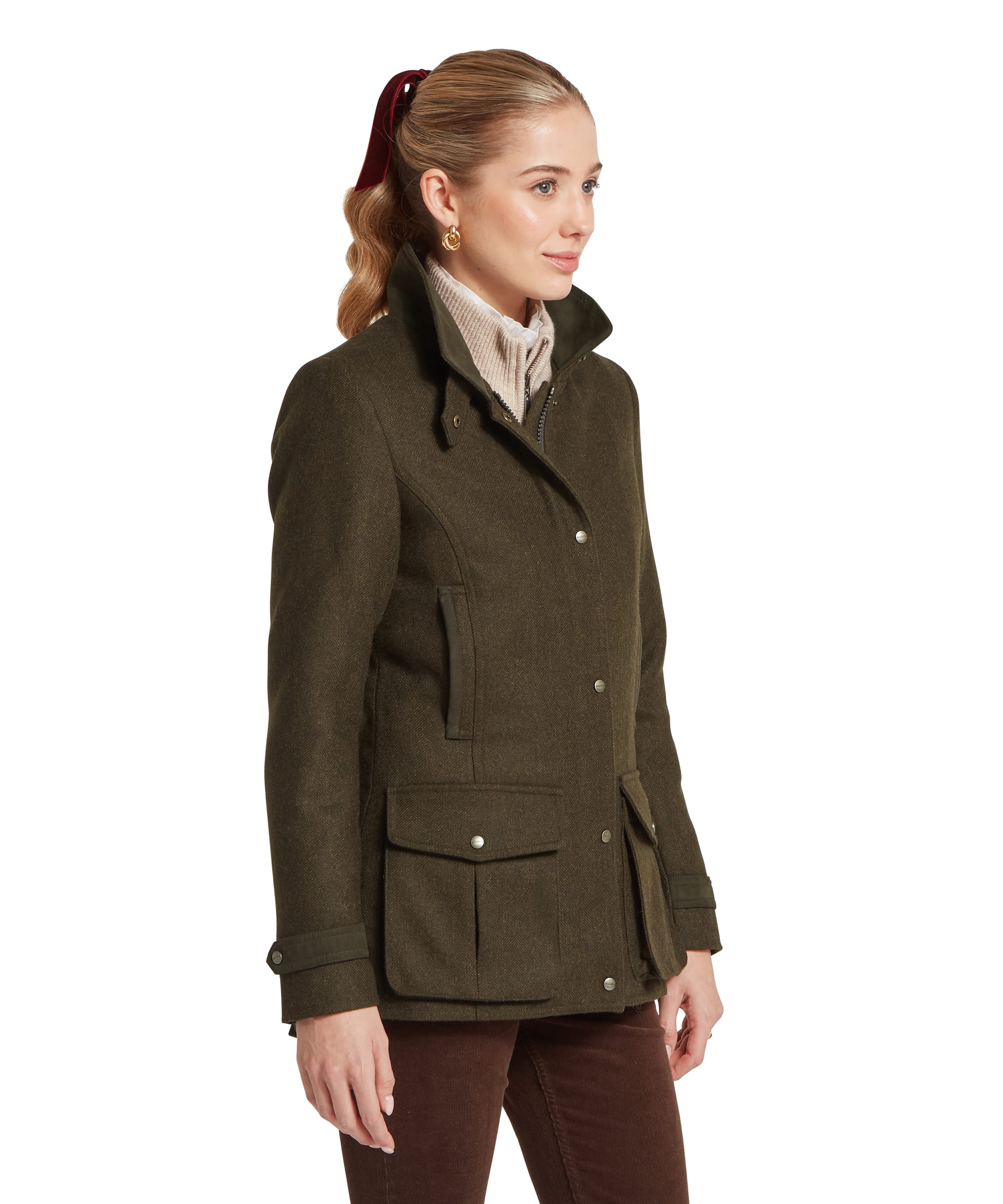 Three-quarter view of a woman wearing the Schöffel Women's Murra Tweed Coat in Dark Olive Herringbone, showing the tailored silhouette, patch pockets with snap fastening, chest pocket and storm collar, layered over a cream roll neck and dark cord trousers