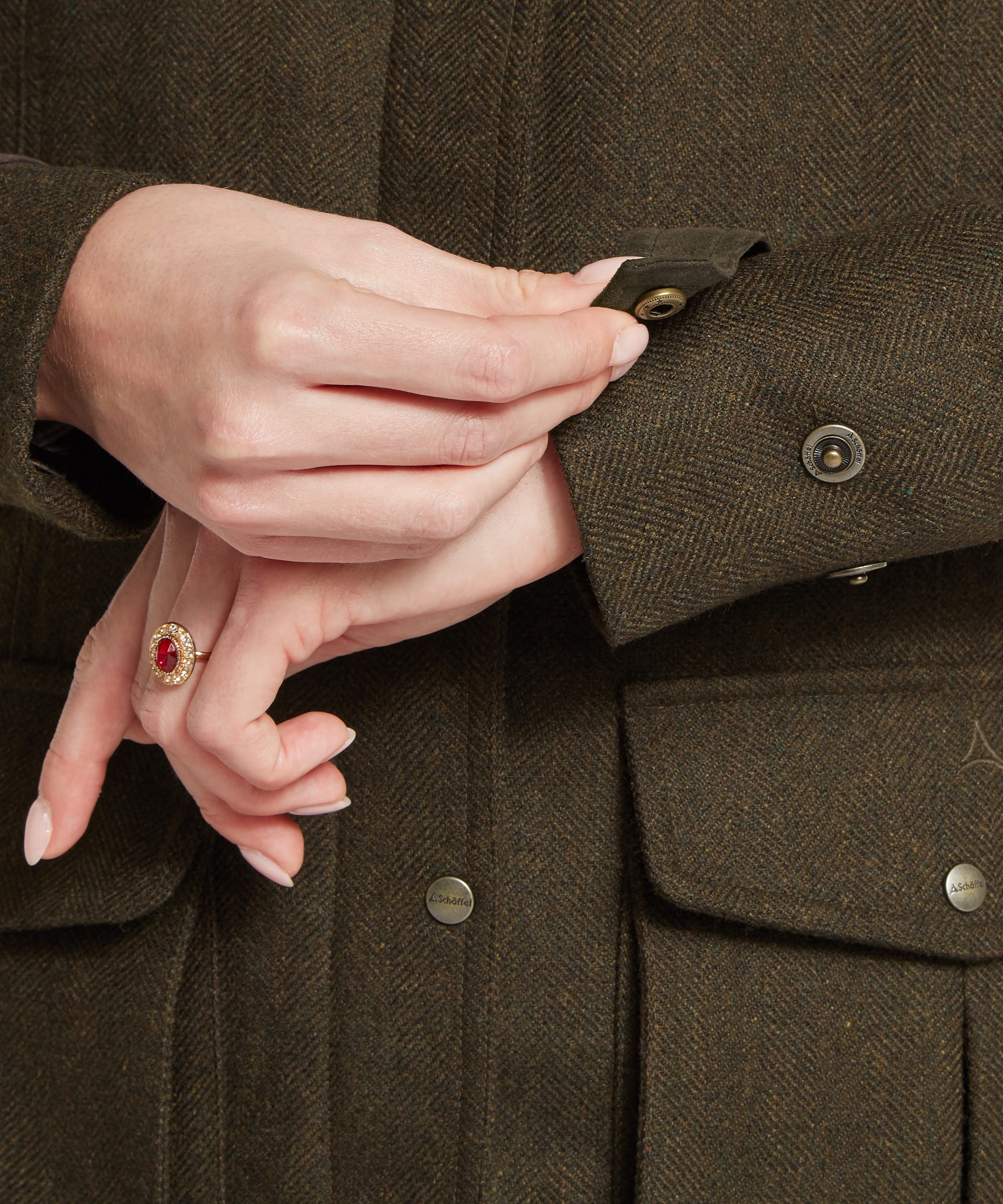 Close-up detail of the cuff and front button fastening of the Women's Schöffel Murra Tweed Coat in dark olive herringbone, showing the antiqued Schöffel branded press stud, patch pockets and the rich herringbone tweed texture.