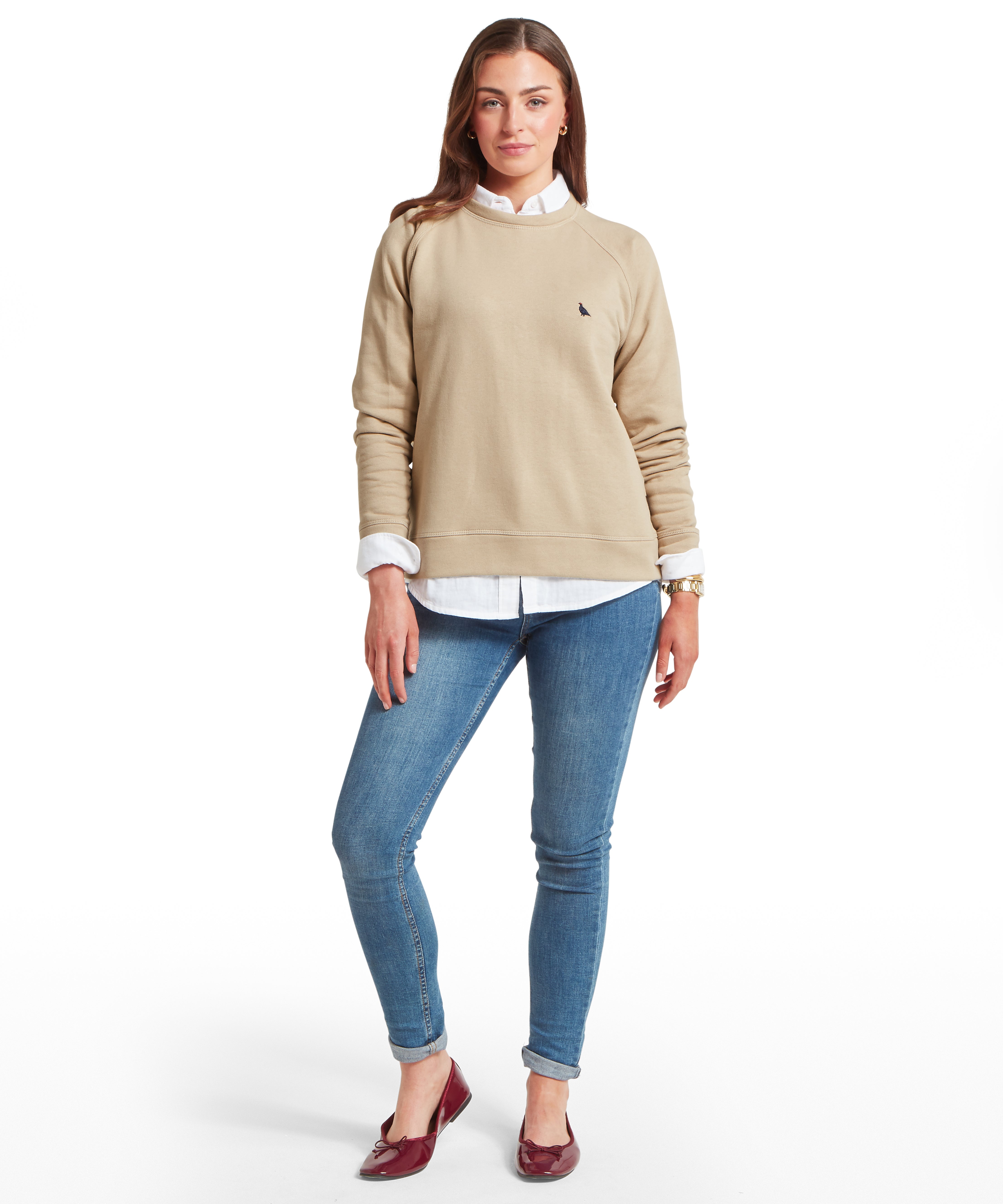 Woman wearing a beige sweatshirt, white shirt, and blue jeans on a white background