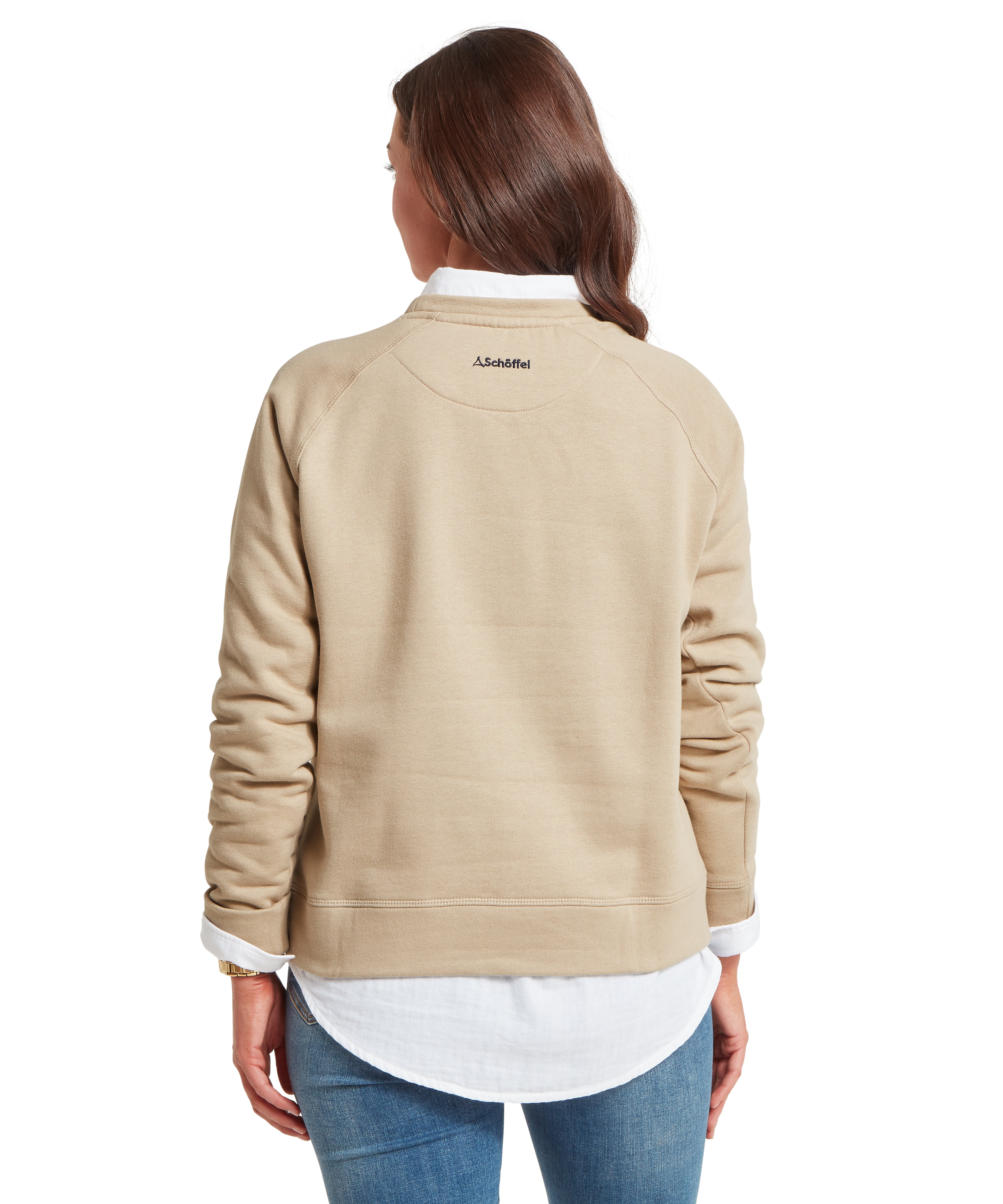 Back view of a person wearing a beige long-sleeve sweatshirt layered over a white collared shirt, with the shirt’s hem and cuffs visible. The sweatshirt features small text near the upper back that reads "Schöffel." Paired with blue jeans, the individual has long, straight brown hair and is posed against a plain white background.