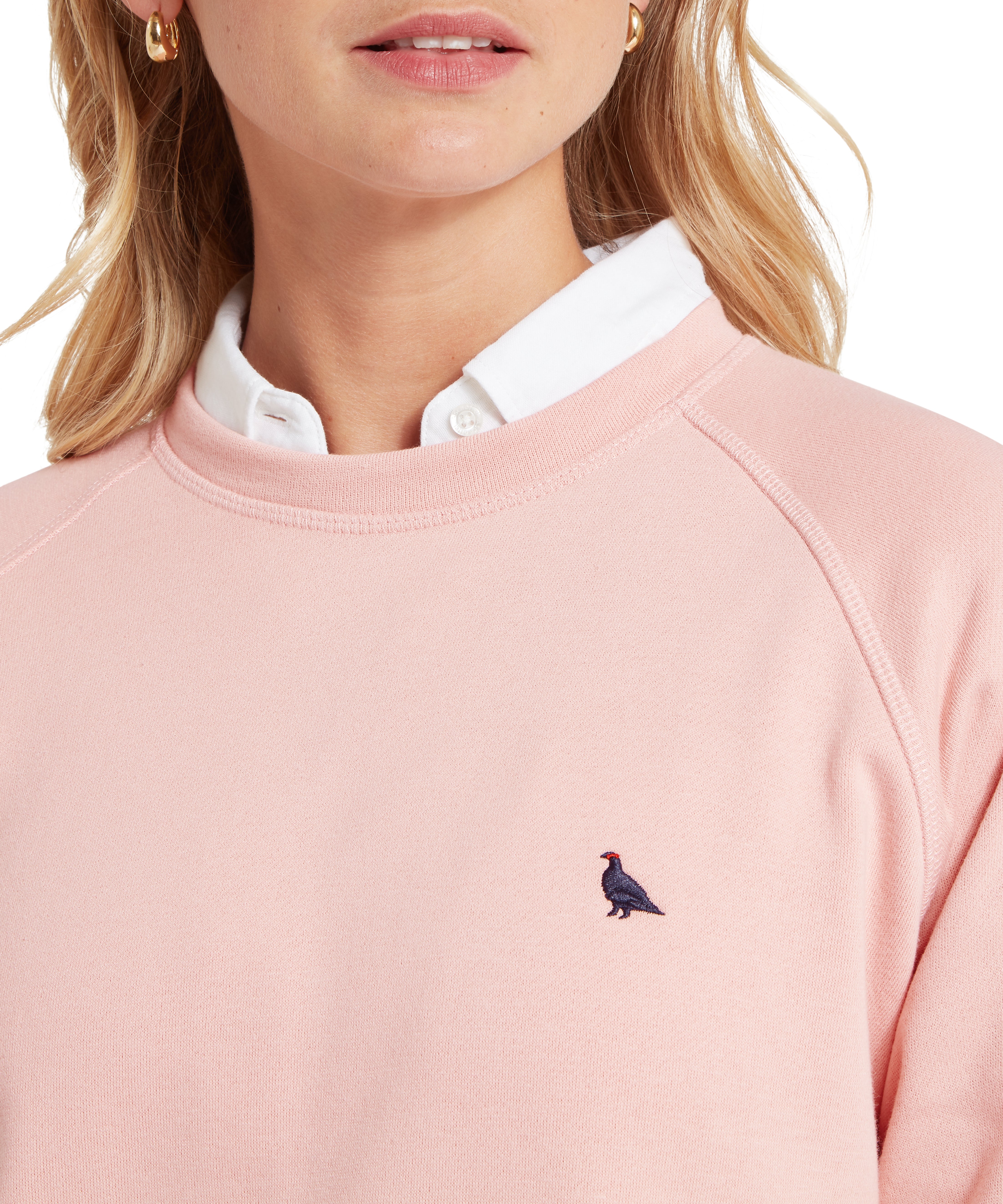 Pink sweatshirt with a small ptarmigan bird emblem worn by a person, close-up on a white background