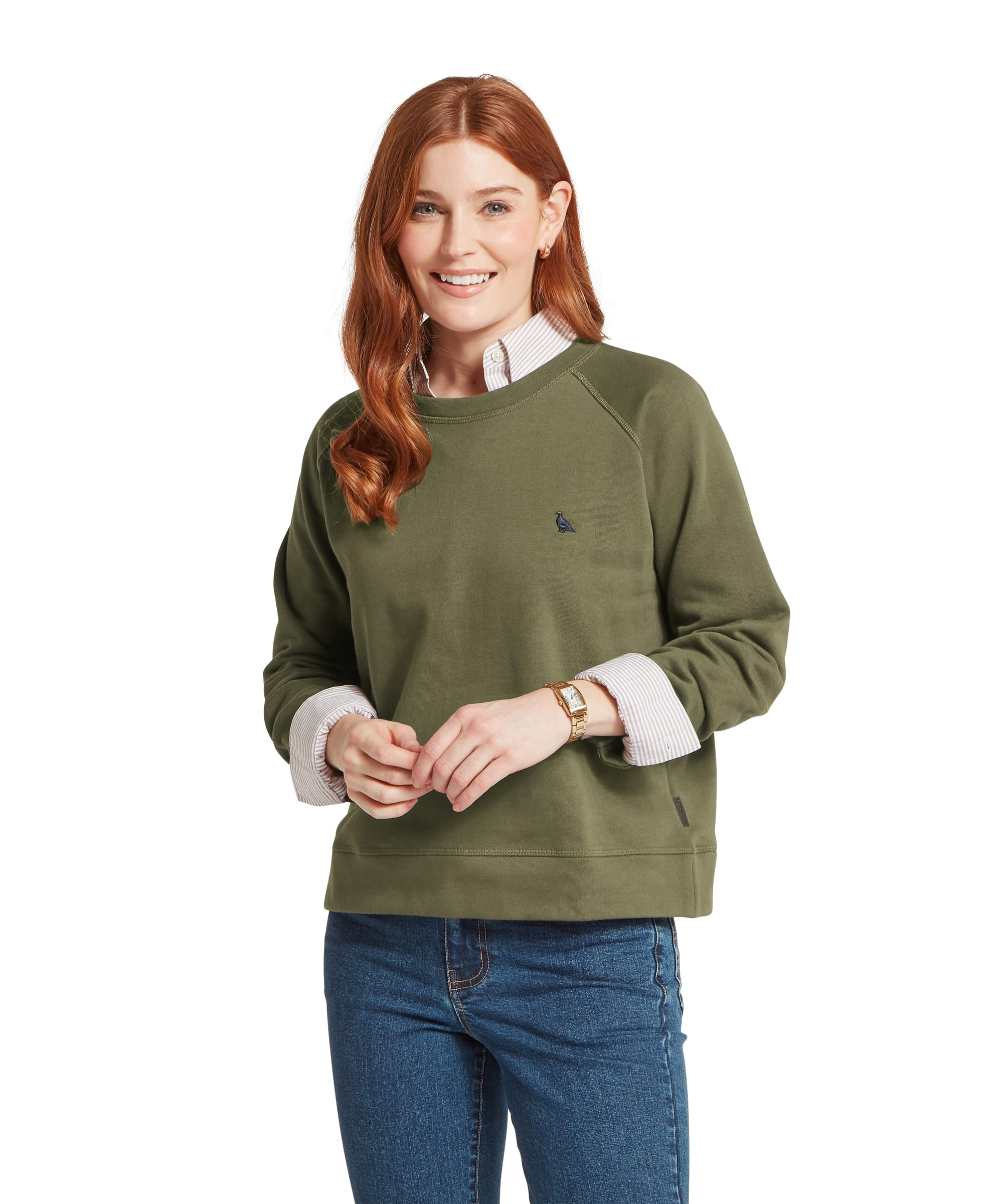 Woman wearing the Schöffel Women's Newberry Sweatshirt in Khaki Green over a striped shirt, featuring the embroidered Schöffel bird logo, raglan sleeves and ribbed hem, styled with blue jeans