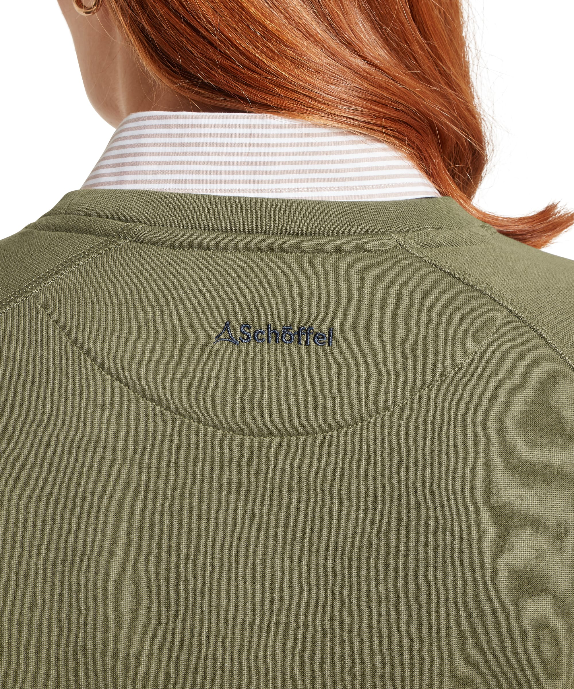 Close-up of the back neck on the Schöffel Women's Newberry Sweatshirt in Khaki Green, highlighting the embroidered Schöffel logo, raglan seam detail and soft cotton fabric, layered over a striped shirt collar