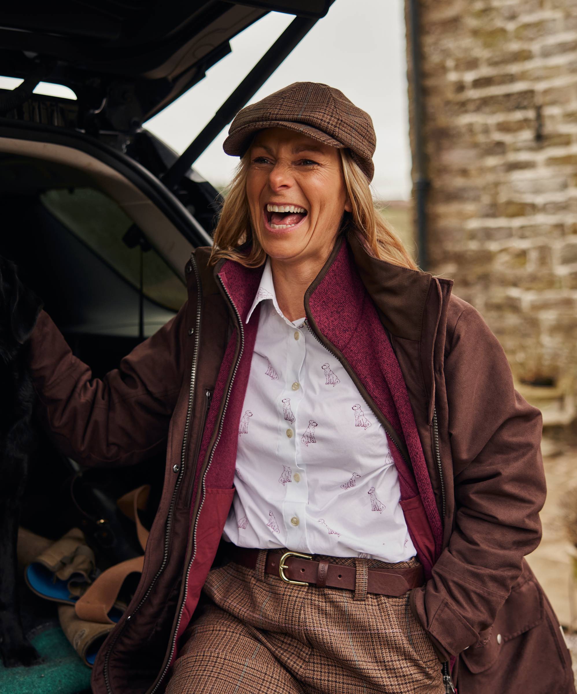 Woman in outdoor attire standing next to a vehicle with a brick wall background