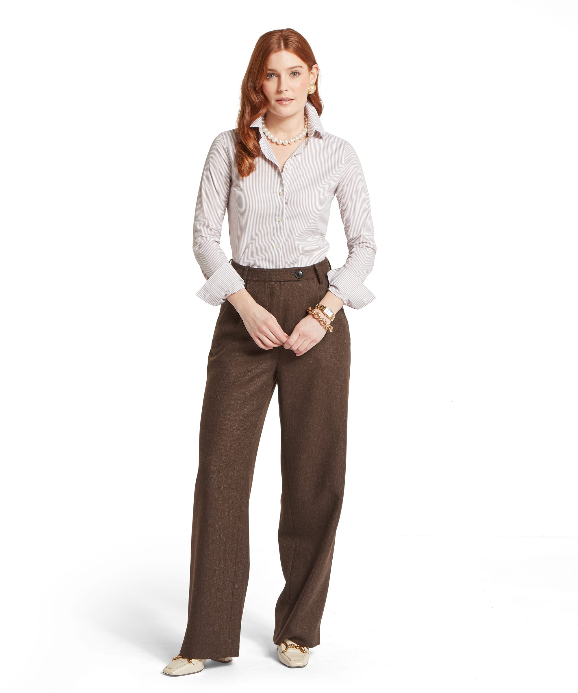 Full-length front view of a woman wearing the Schöffel Women's Norfolk Shirt in Stone, styled with wide-leg brown herringbone tweed trousers, a pearl necklace and gold horsebit loafers for a refined country occasion look
