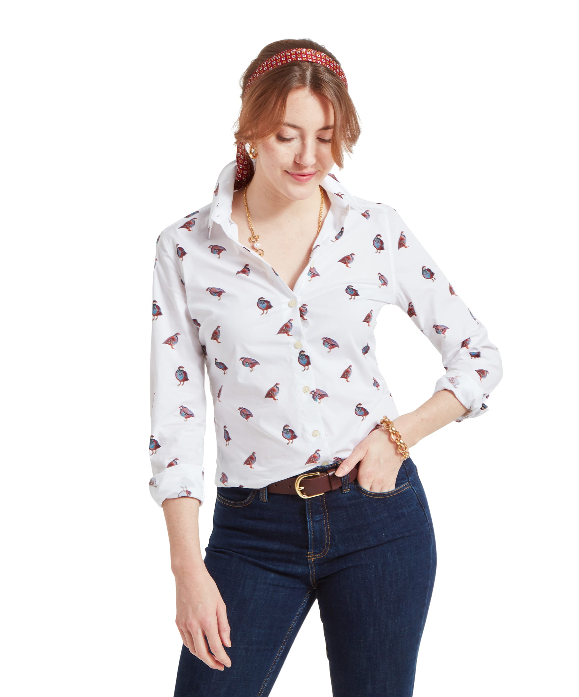 A woman is wearing a Schöffel Norfolk Shirt for Womens in Brown White with a pattern of partridge birds. She has light brown hair styled in a low bun with a red patterned headband. She is smiling slightly and has her hands casually resting in her pockets.