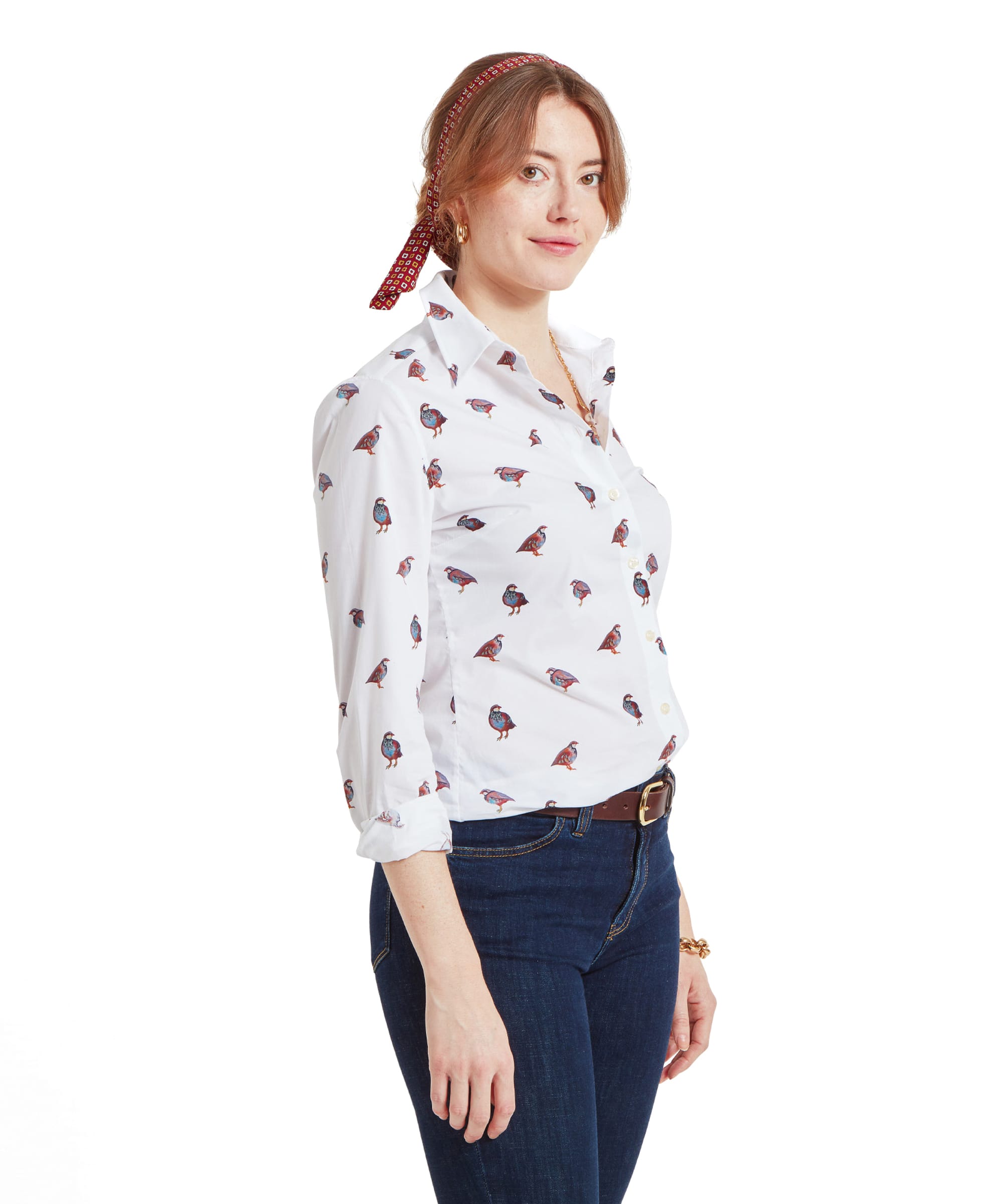 A side view of a woman wearing a Schöffel Norfolk Shirt for Womens in Brown White with a partridge bird pattern, dark blue jeans, and a red headband. Her light brown hair is tied back, and she is looking slightly to the side.
